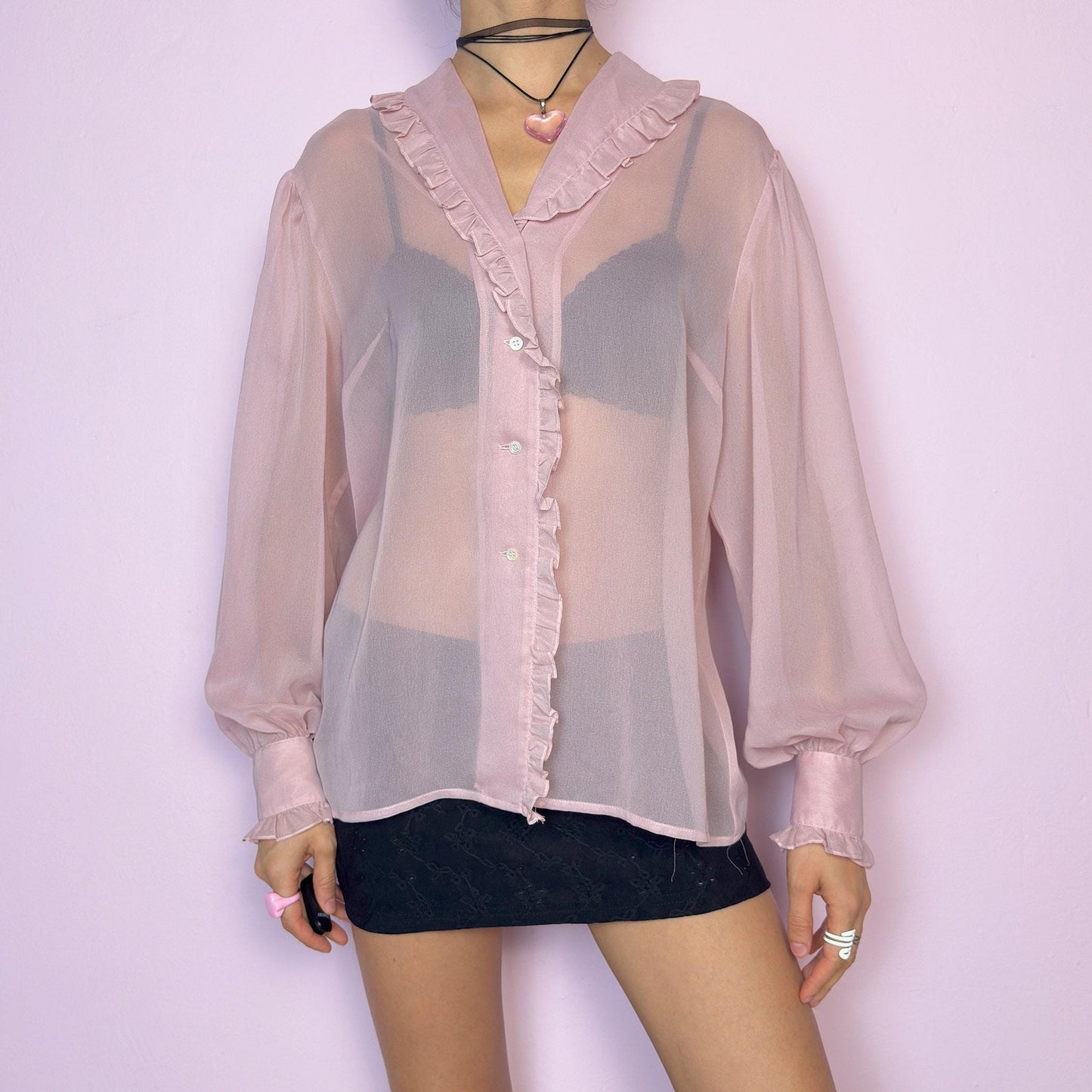 The Vintage Pink Ruffle Sheer Blouse features a romantic and ethereal silhouette with soft, see-through fabric and delicate ruffle trim along the collar and button placket. The flowy cut and voluminous sleeves with buttoned cuffs add a dreamy charm. Perfect for layering for a soft coquette aesthetic. Made in France. Excellent vintage condition. adult world shop