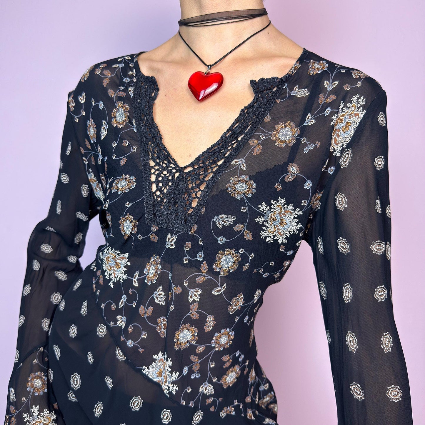 The Y2K Asymmetric Bell Sleeve Top is a vintage 2000s piece featuring a sheer black floral print with an asymmetric hem and dramatic bell sleeves for a flowy silhouette. The deep V-neckline is accented with crochet lace trim for a romantic touch. Lightweight and breathable, it’s perfect for summer layering or festival styling. Includes long sleeves with a bell flare for an elegant witchy vibe. Great vintage condition. adult world shop