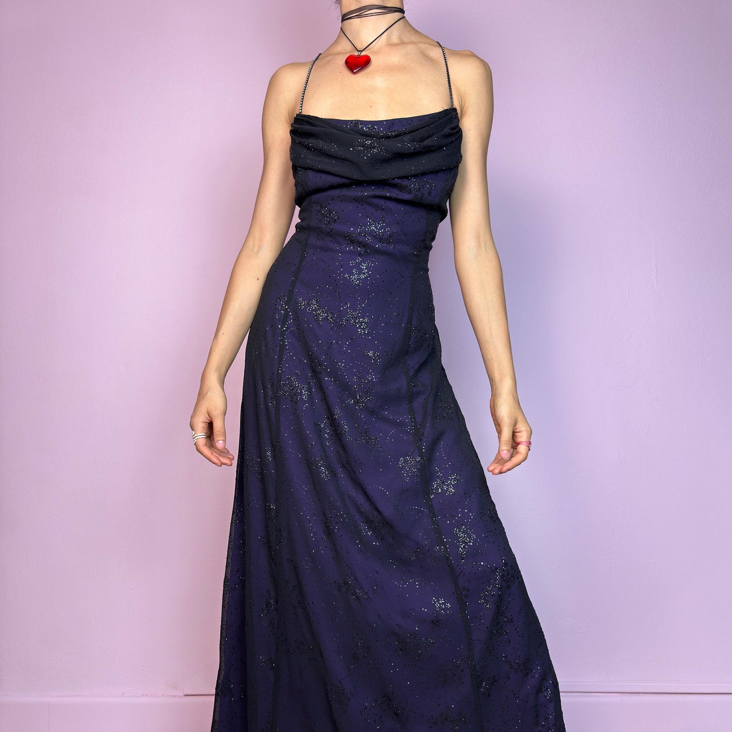 Step into the night in this breathtaking vintage 90s formal black glitter maxi dress. Crafted from a deep purple base with a sheer black overlay, it features all-over subtle glitter details that catch the light with every move. The draped cowl neckline adds soft elegance, while the delicate spaghetti straps are adorned with shimmering rhinestones for that extra sparkle. Designed with a flattering fit and a back zipper closure for ease and shape. A rare celestial piece – ideal for prom.