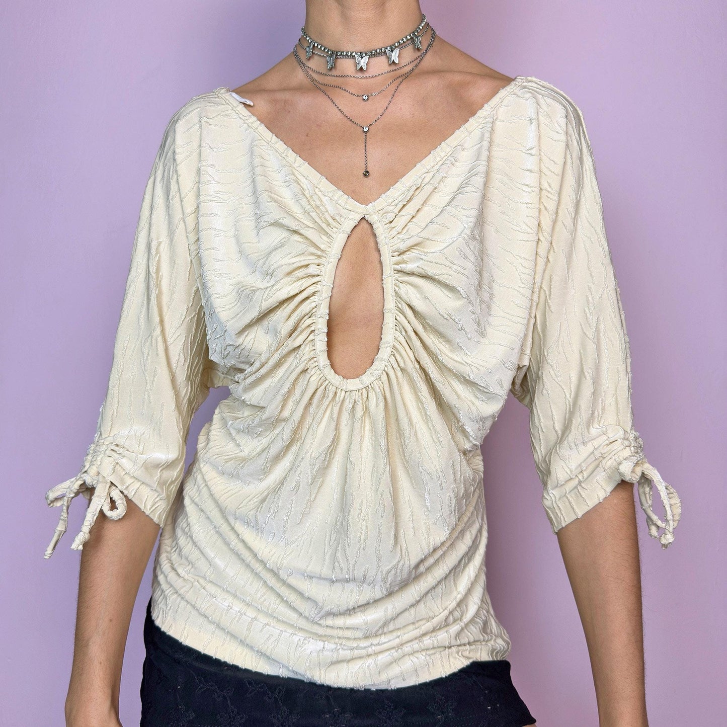 The Y2K Ruched Keyhole Top is a vintage 2000s piece crafted from a textured, stretchy fabric in a pale yellowish cream tone. Features a flattering gathered bust with a keyhole cutout, V-neckline, and soft drape. The three-quarter sleeves are finished with delicate tie details for an adjustable fit. Perfect for summer days and casual dates. Made in Spain. Excellent vintage condition. adult world shop