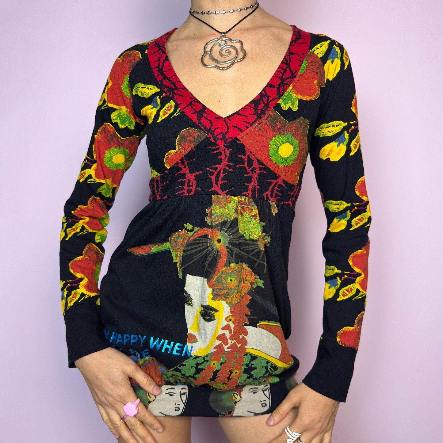 The Y2K Desigual Graphic Print Top is a rare vintage 2000s long sleeve top by Desigual featuring an eclectic mix of prints and bold colors. This artsy piece combines floral motifs, illustrated portraits, and poetic text layered over a stretchy black base. Designed with a deep V-neckline and empire waist for a flattering silhouette. The bottom hem is subtly gathered for a closer fit, giving it a mini dress vibe. Includes hidden side pockets. adult world shop