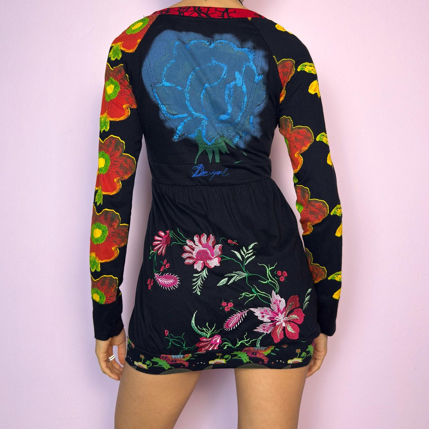 The Y2K Desigual Graphic Print Top is a rare vintage 2000s long sleeve top by Desigual featuring an eclectic mix of prints and bold colors. This artsy piece combines floral motifs, illustrated portraits, and poetic text layered over a stretchy black base. Designed with a deep V-neckline and empire waist for a flattering silhouette. The bottom hem is subtly gathered for a closer fit, giving it a mini dress vibe. Includes hidden side pockets. adult world shop