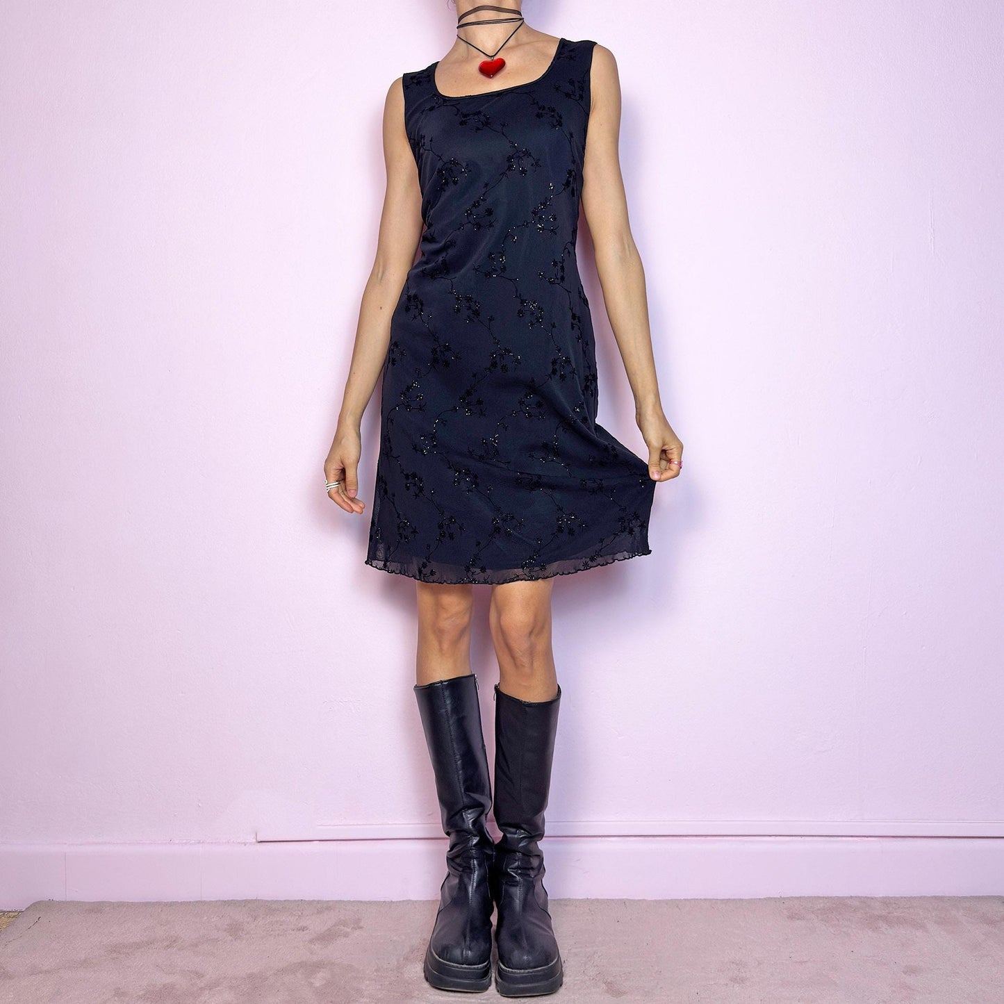 The Vintage 90s Black Mesh Mini Dress is a delicate and stretchy black mini dress featuring sheer mesh overlay with velvet floral embroidery and subtle glitter accents. Designed with a flattering sleeveless silhouette, scoop neckline, and lettuce hem for a soft romantic touch. Perfect for witchy party looks, 90s glam nights, or layering with grunge accessories. Made in UK. Excellent vintage condition.
