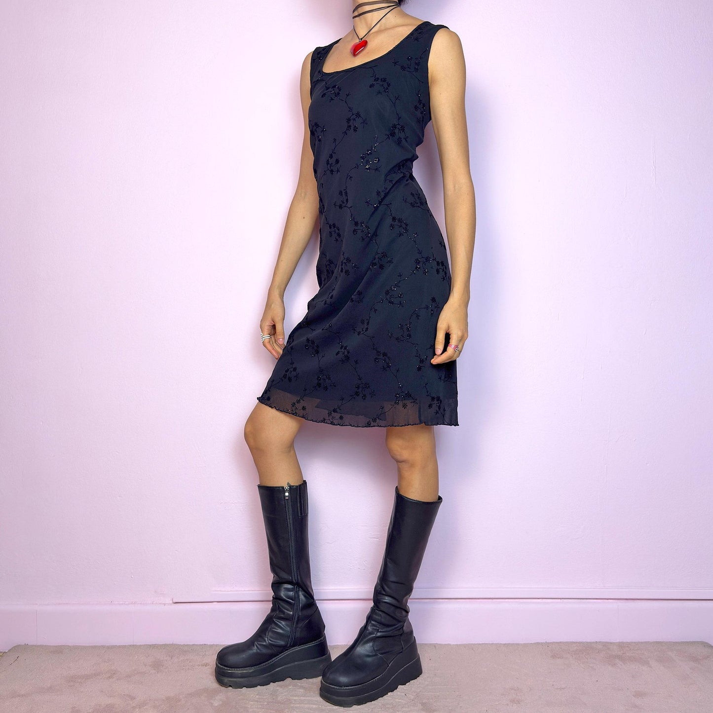 The Vintage 90s Black Mesh Mini Dress is a delicate and stretchy black mini dress featuring sheer mesh overlay with velvet floral embroidery and subtle glitter accents. Designed with a flattering sleeveless silhouette, scoop neckline, and lettuce hem for a soft romantic touch. Perfect for witchy party looks, 90s glam nights, or layering with grunge accessories. Made in UK. Excellent vintage condition.