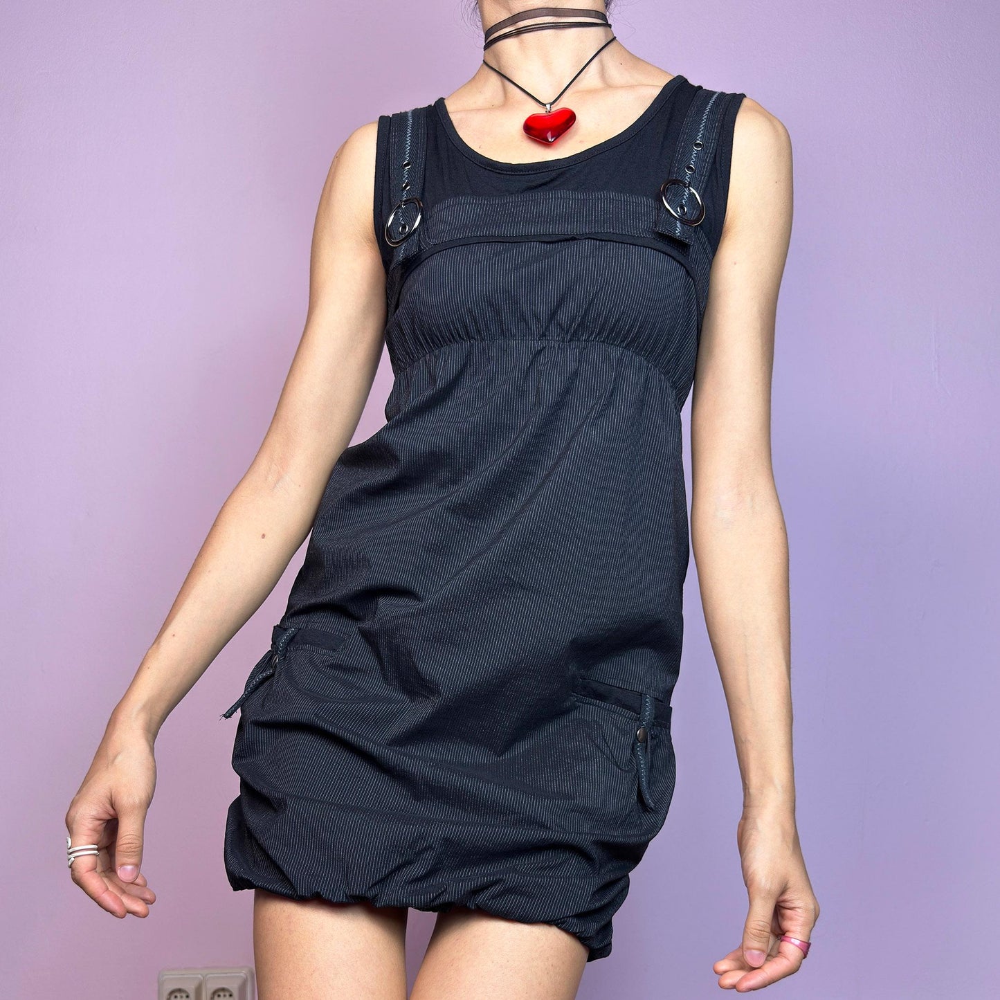The Y2K Black Striped Bubble Mini Dress is a rare vintage 2000s piece with a playful techwear vibe. Features subtle vertical pinstripes, silver-tone D-rings on the straps, and functional side pockets. The ruched bubble hem adds volume and edge, while the stretchy fabric and empire waist provide a flattering fit. Finished with a side zipper closure for easy wear. Perfect for cybercore, Y2K streetwear, or Harajuku-inspired looks. Excellent vintage condition.