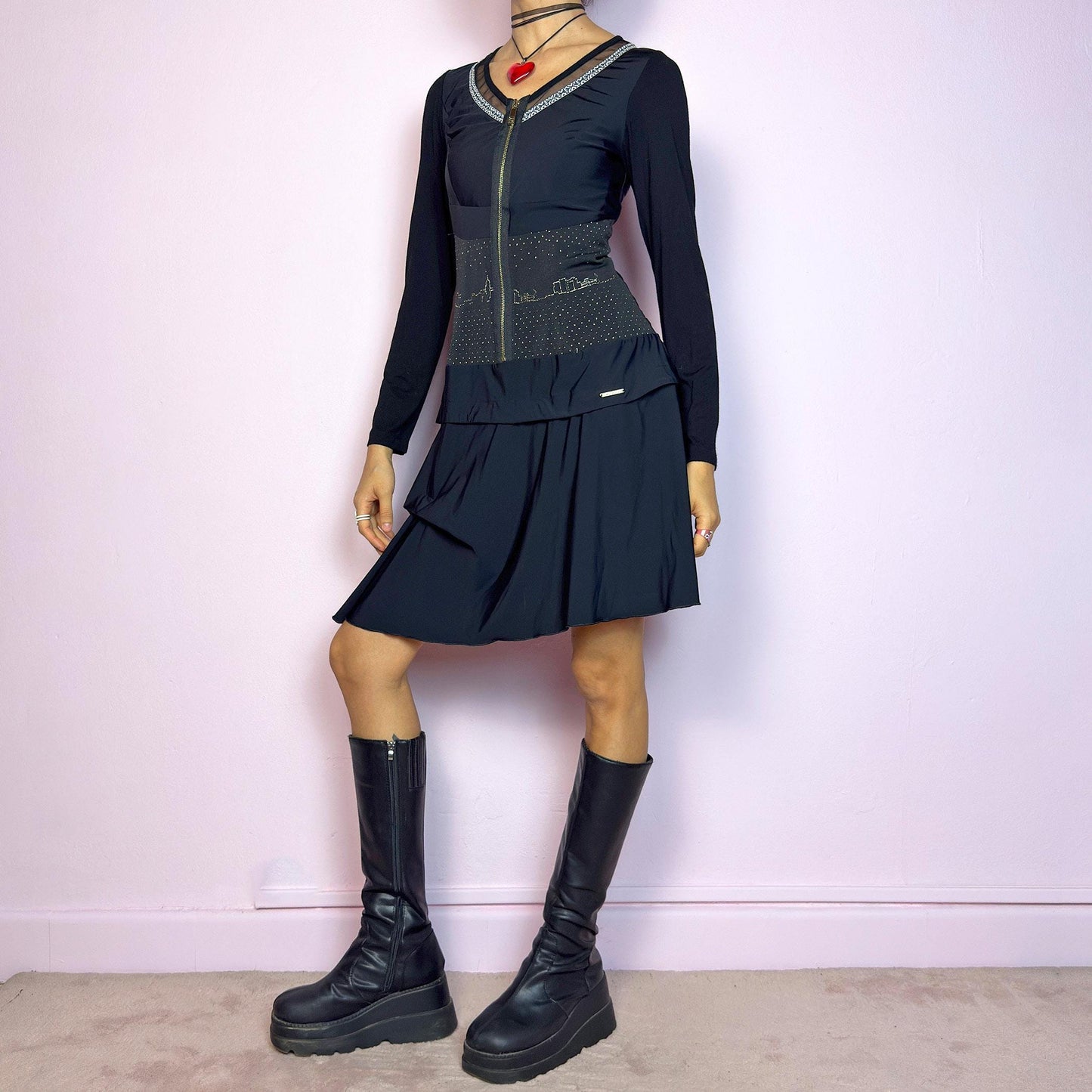 The Y2K Black Long Sleeve Mini Dress is a vintage 2000s sleek and deconstructed mini dress featuring a fitted bodice with a front zipper and a glittery cityscape detail at the waist. The long sleeves balance the edgy vibe of the layered, asymmetrical skirt, giving it a sculptural silhouette. Stretchy and comfortable, this dress is perfect for cybercore and futuristic clubwear. Great vintage condition.