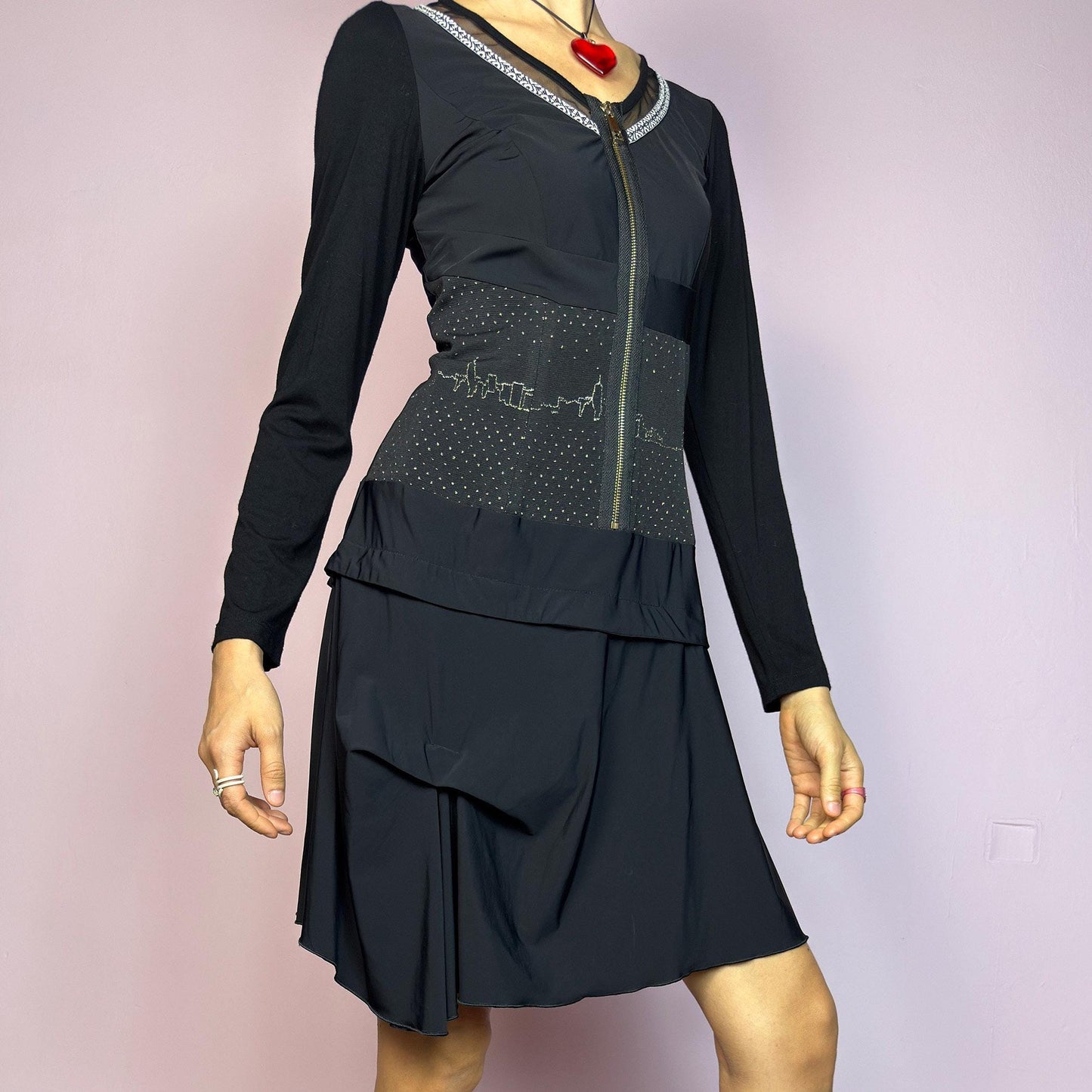 The Y2K Black Long Sleeve Mini Dress is a vintage 2000s sleek and deconstructed mini dress featuring a fitted bodice with a front zipper and a glittery cityscape detail at the waist. The long sleeves balance the edgy vibe of the layered, asymmetrical skirt, giving it a sculptural silhouette. Stretchy and comfortable, this dress is perfect for cybercore and futuristic clubwear. Great vintage condition.