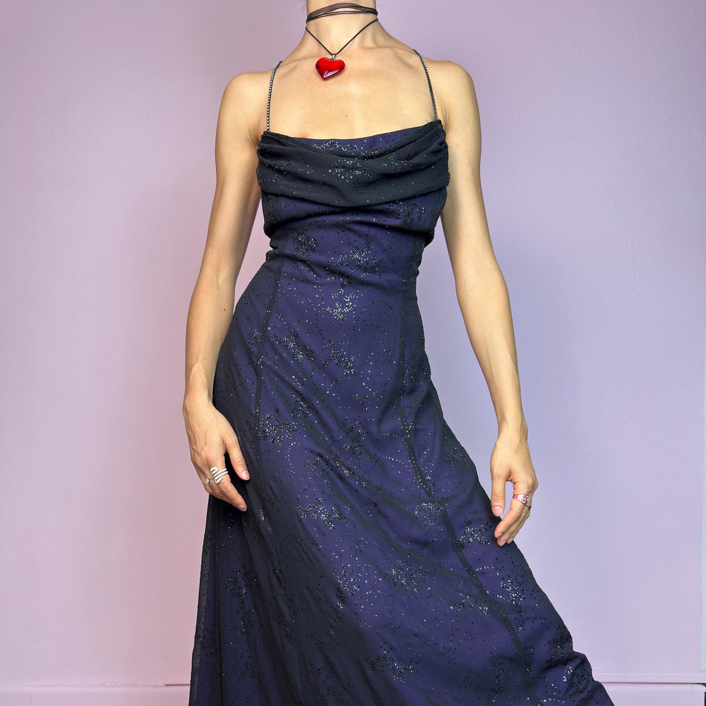Step into the night in this breathtaking vintage 90s formal black glitter maxi dress. Crafted from a deep purple base with a sheer black overlay, it features all-over subtle glitter details that catch the light with every move. The draped cowl neckline adds soft elegance, while the delicate spaghetti straps are adorned with shimmering rhinestones for that extra sparkle. Designed with a flattering fit and a back zipper closure for ease and shape. A rare celestial piece – ideal for prom.