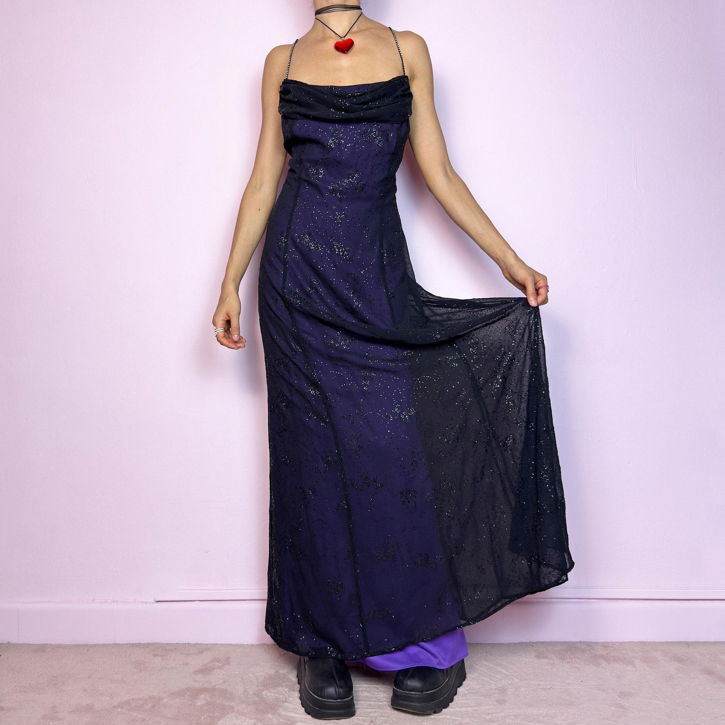 Step into the night in this breathtaking vintage 90s formal black glitter maxi dress. Crafted from a deep purple base with a sheer black overlay, it features all-over subtle glitter details that catch the light with every move. The draped cowl neckline adds soft elegance, while the delicate spaghetti straps are adorned with shimmering rhinestones for that extra sparkle. Designed with a flattering fit and a back zipper closure for ease and shape. A rare celestial piece – ideal for prom.