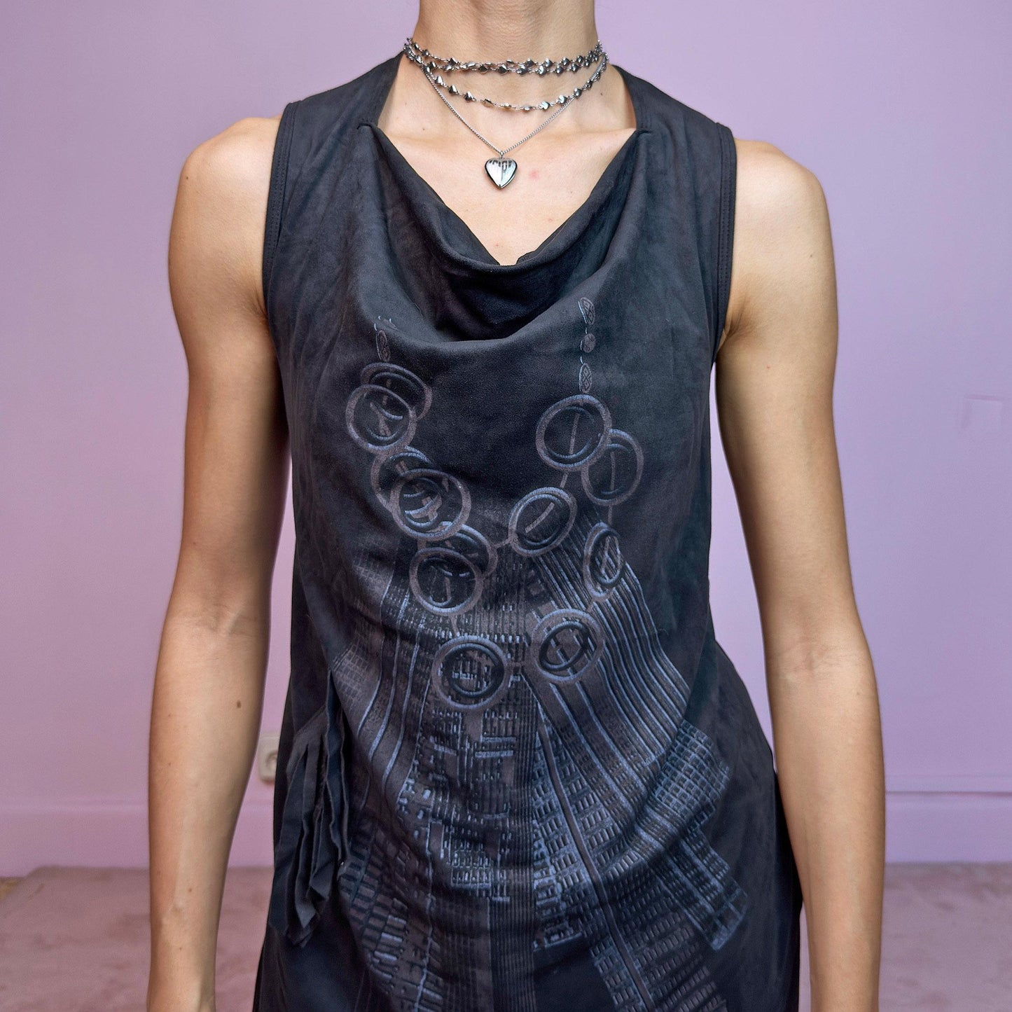 The Y2K Black Asymmetric Mini Dress is a futuristic and artsy vintage 2000s mini dress featuring a unique cowl neckline and layered asymmetric hem. Crafted from soft black stretchy fabric with a subtle suede-like texture, it showcases an abstract tech-inspired print on the front. The sleeveless design and fluid silhouette make it ideal for edgy, experimental, or cyber fairy looks. A true statement piece with avant-garde flair. Excellent vintage condition.
