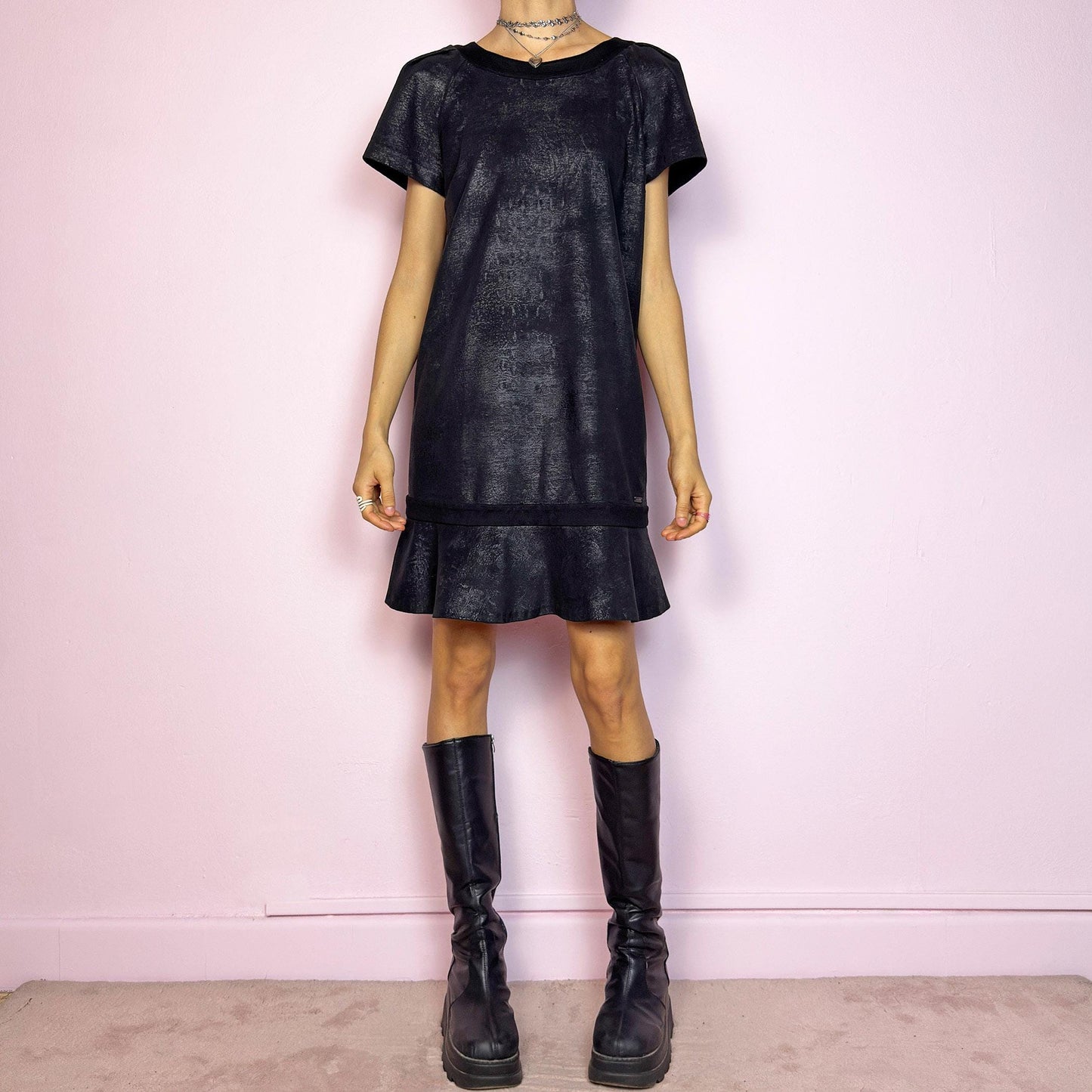The Y2K Black Cop Copine Dress is a sleek and structured mini dress with subtle futuristic flair. Made from a soft black fabric with a slight sheen and textured abstract finish, it features short sleeves, a relaxed straight silhouette, and a ruffled hem for added movement. The back showcases a bold V-cut detail with a button closure at the neck. Unique yet minimalist, perfect for modern grunge or avant-garde looks. Made in Portugal. Excellent vintage condition.