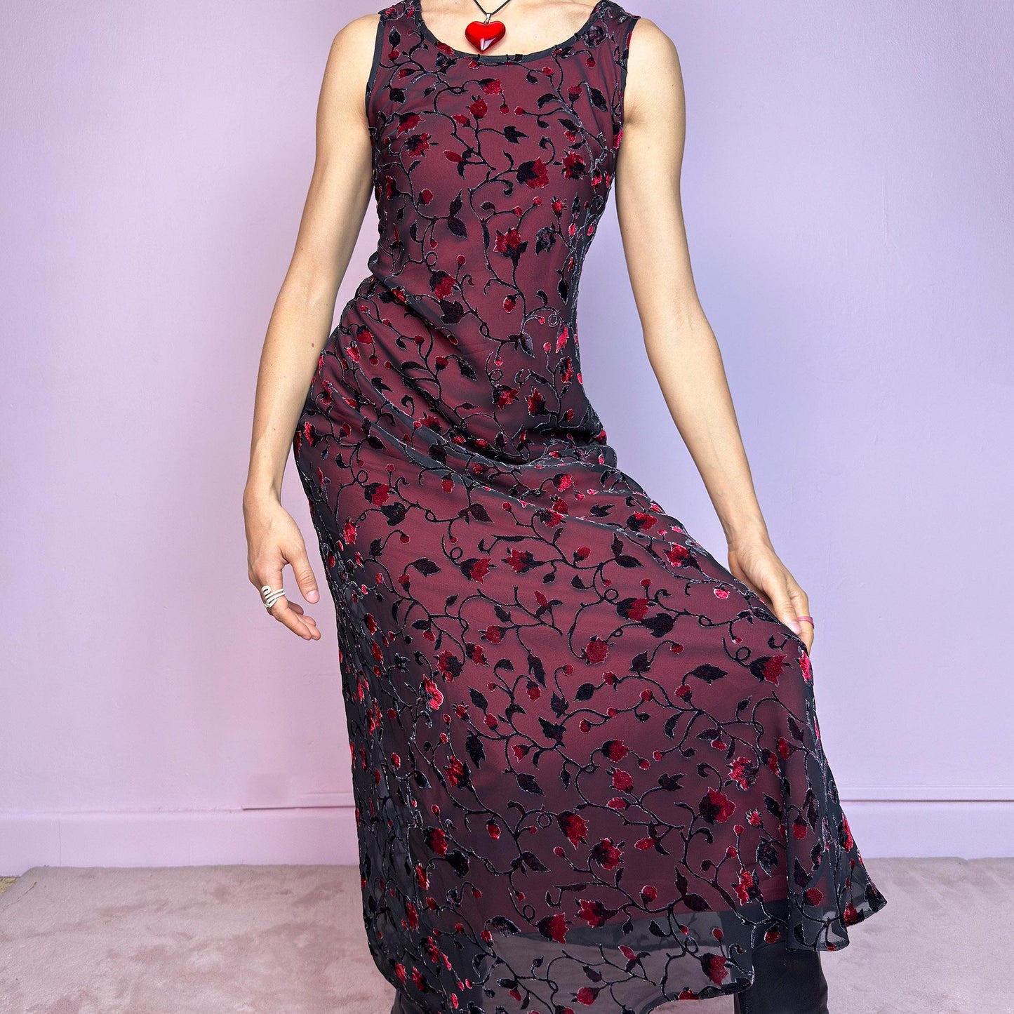 The Vintage 90s Black Sheer Floral Midi Dress is a striking piece featuring a sheer black overlay with textured velvet floral details layered over a vibrant red lining. The sleeveless design and round neckline offer a timeless silhouette, while the fitted shape and midi length create a flattering, romantic look. The fabric is slightly stretchy and flowy, with a gothic romantic vibe perfect for dark fairycore, witchy looks, or 2000s party aesthetics. Excellent vintage condition.