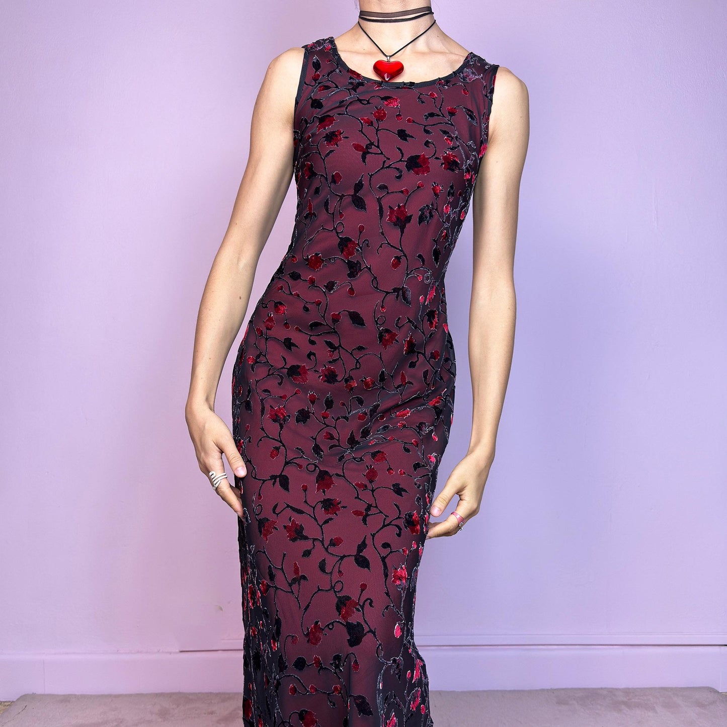 The Vintage 90s Black Sheer Floral Midi Dress is a striking piece featuring a sheer black overlay with textured velvet floral details layered over a vibrant red lining. The sleeveless design and round neckline offer a timeless silhouette, while the fitted shape and midi length create a flattering, romantic look. The fabric is slightly stretchy and flowy, with a gothic romantic vibe perfect for dark fairycore, witchy looks, or 2000s party aesthetics. Excellent vintage condition.