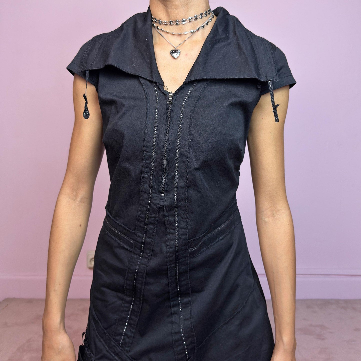 This vintage 2000s black techwear dress features cap sleeves, a dramatic asymmetric hem, and sculptural paneling for a bold silhouette. Made from a stretchy fabric, it includes a side zip closure and ruched utility pocket. Decorative topstitching and a funnel-style collar with drawstrings elevate the structure. Mid-length and lightweight, perfect for summer. A sleek statement in futuristic edge. Great vintage condition.
