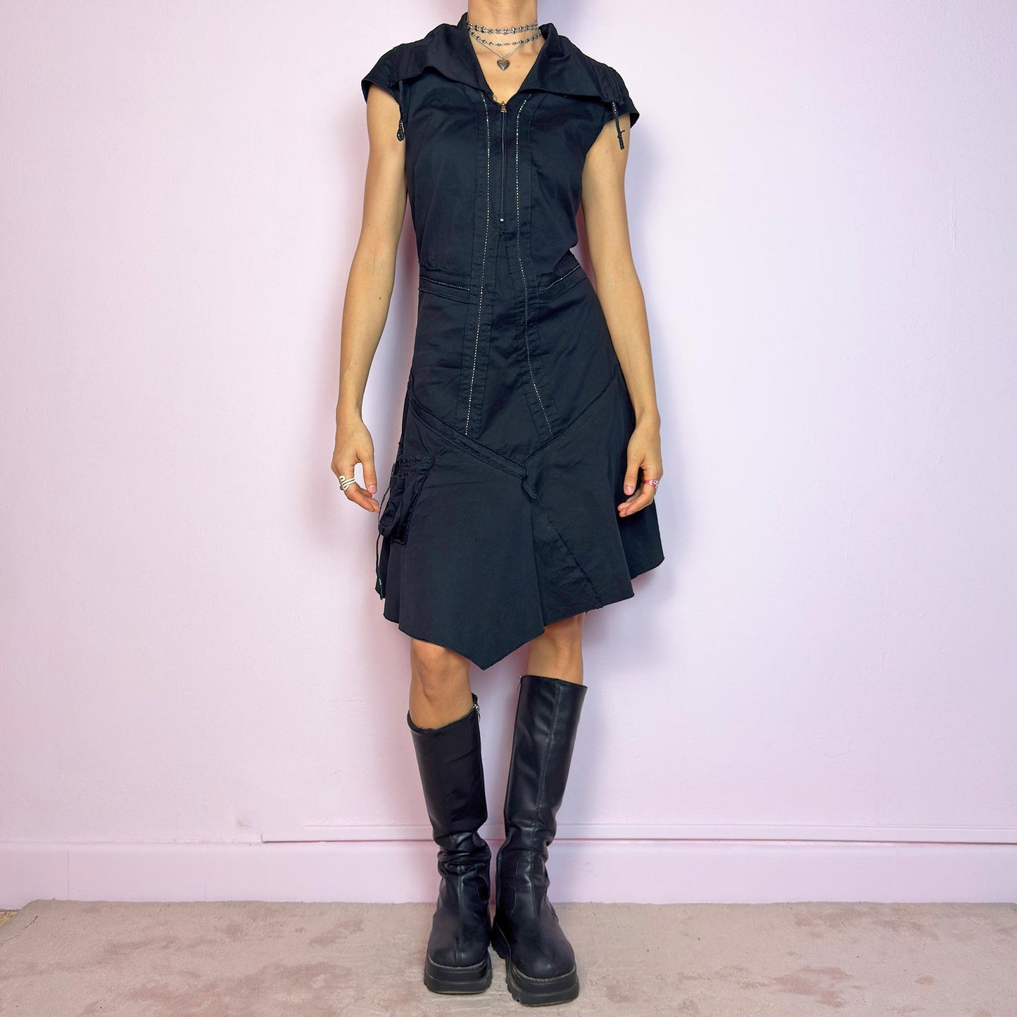 This vintage 2000s black techwear dress features cap sleeves, a dramatic asymmetric hem, and sculptural paneling for a bold silhouette. Made from a stretchy fabric, it includes a side zip closure and ruched utility pocket. Decorative topstitching and a funnel-style collar with drawstrings elevate the structure. Mid-length and lightweight, perfect for summer. A sleek statement in futuristic edge. Great vintage condition.