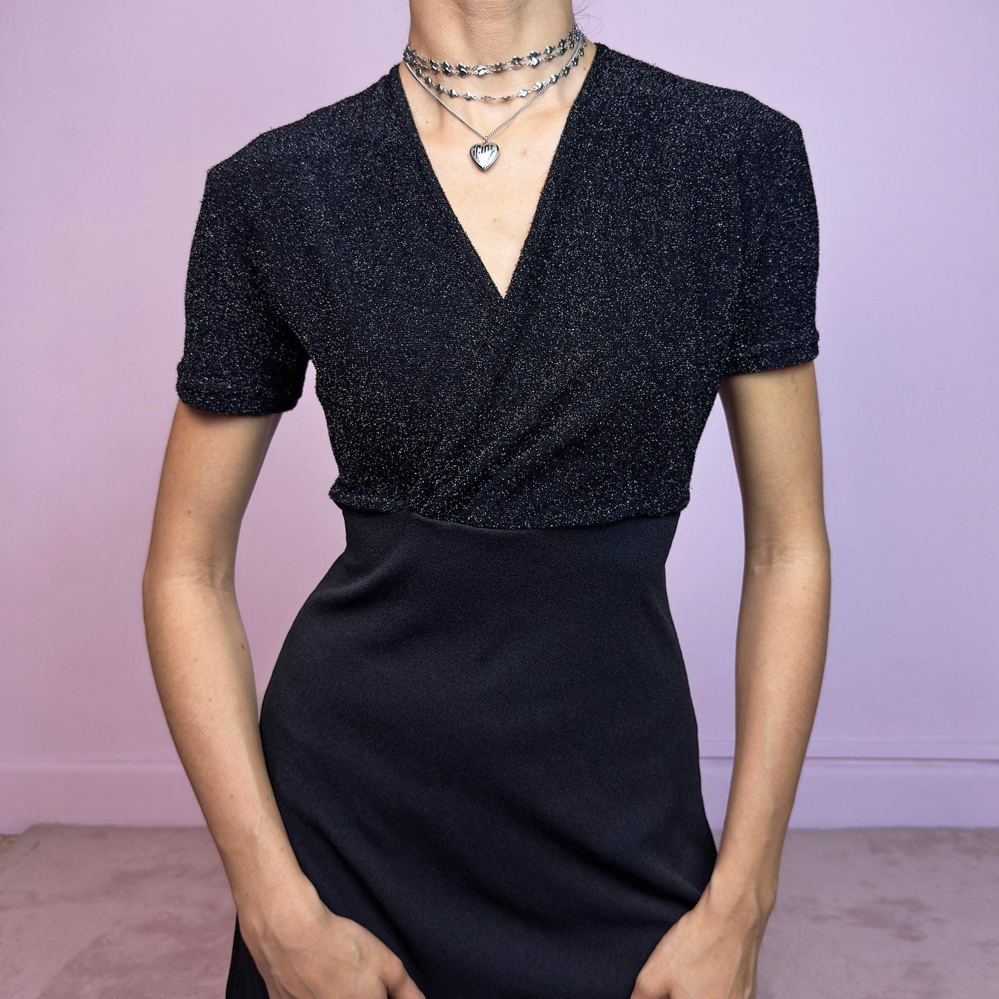 This vintage 90s black mini dress features a glitter-knit wrap bodice with short sleeves and a deep V-neckline. The matte black skirt contrasts with a subtle shimmer and ties at the back for a cinched waist. The stretchy fabric molds to the body while maintaining structure. Its above-knee length makes it ideal for summer nights or party wear. A quiet classic with minimalist drama and nostalgic allure. Made in France. Great vintage condition.