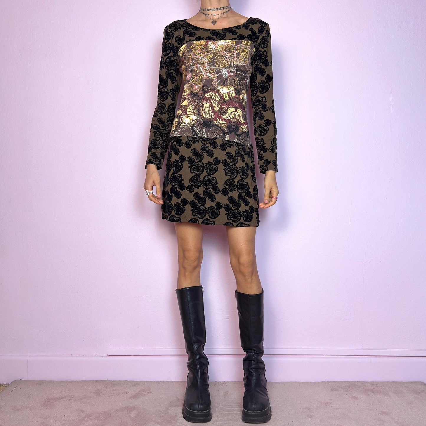 The Y2K Printed Velvet Mini Dress is a striking and artsy vintage piece from the 2000s. This stretchy mini dress features a unique mixed-media design with an abstract print panel at the chest, contrasted by a brown base covered in bold black velvet flocked florals. With its long sleeves, slightly flared hem, and figure-hugging silhouette, it's perfect for maximalist layering or making a statement on its own. A rare cyber-romantic gem for experimental, alt, or fairy-grunge wardrobes.