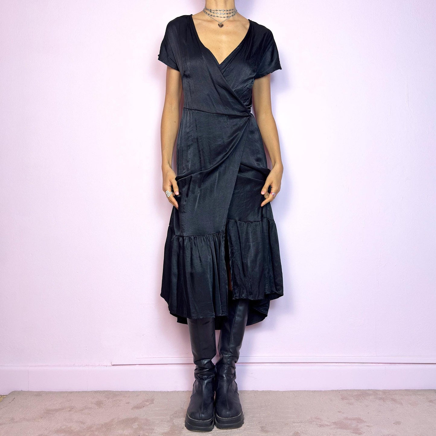 This vintage 2000s black wrap midi dress is made from a satin-style fabric with a soft sheen and airy drape. It features short sleeves, a plunging V-neckline, and an adjustable tie closure at the back. The hem is finished with a gathered ruffle panel, adding movement and shape. Perfect for elegant summer nights. A dramatic yet effortless piece with a quietly romantic silhouette.