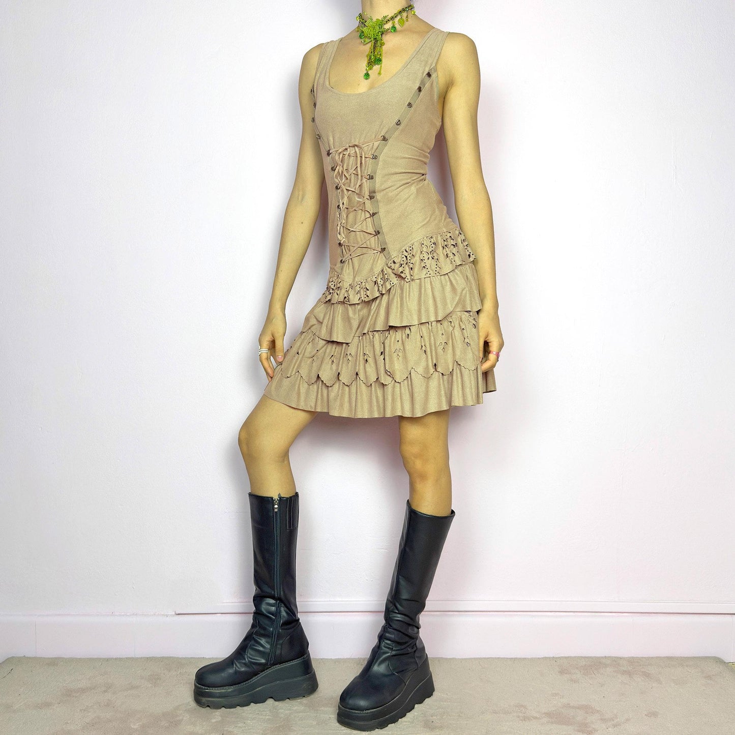 This vintage 2000s mini dress comes in soft beige with a scoop neckline, corset lace-up front, and stretchy fit. The drop waist leads to layered ruffle tiers with eyelet cutouts and scalloped hems. A fairy-meets-western Y2K silhouette—fitted on top, flirty on the bottom. Perfect for casual summer days or standout festival looks. Great vintage condition.