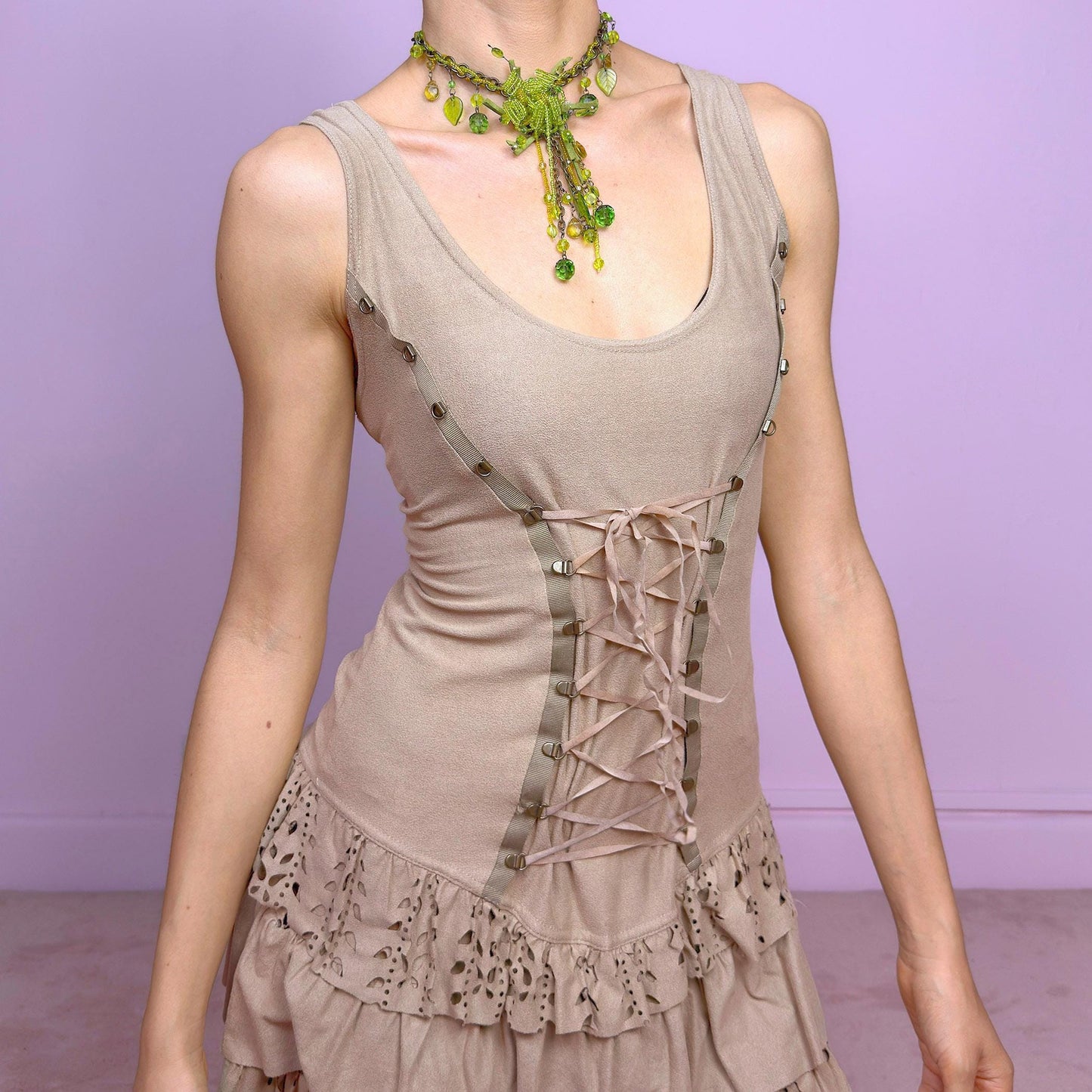 This vintage 2000s mini dress comes in soft beige with a scoop neckline, corset lace-up front, and stretchy fit. The drop waist leads to layered ruffle tiers with eyelet cutouts and scalloped hems. A fairy-meets-western Y2K silhouette—fitted on top, flirty on the bottom. Perfect for casual summer days or standout festival looks. Great vintage condition.