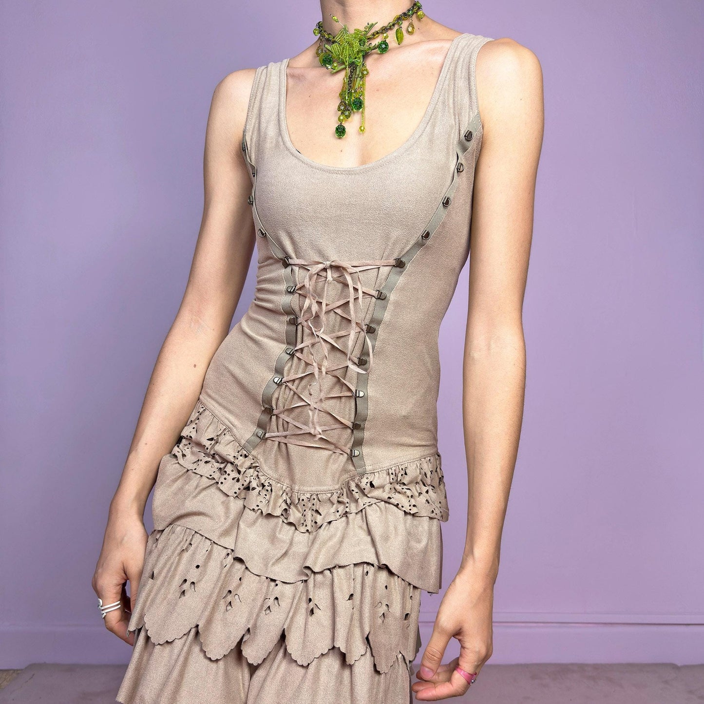 This vintage 2000s mini dress comes in soft beige with a scoop neckline, corset lace-up front, and stretchy fit. The drop waist leads to layered ruffle tiers with eyelet cutouts and scalloped hems. A fairy-meets-western Y2K silhouette—fitted on top, flirty on the bottom. Perfect for casual summer days or standout festival looks. Great vintage condition.