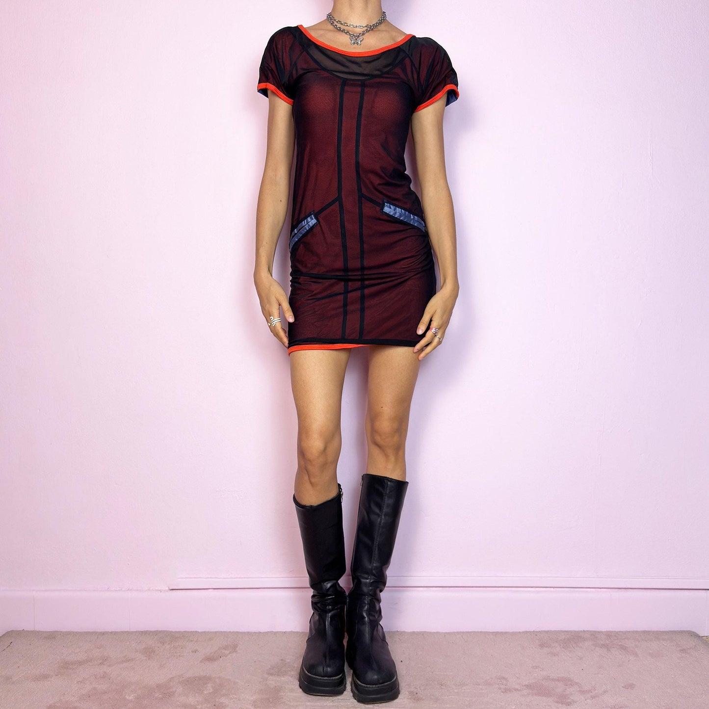 This vintage 2000s mini dress features sheer black mesh over an orange base with blue vertical stripes. Glossy faux-pocket details and neon orange trim add bold contrast. The fitted silhouette includes short sleeves, a scoop neckline, and stretch throughout. A cyber-inspired Y2K piece with futuristic, sporty edge—perfect for summer nights and bold party looks.