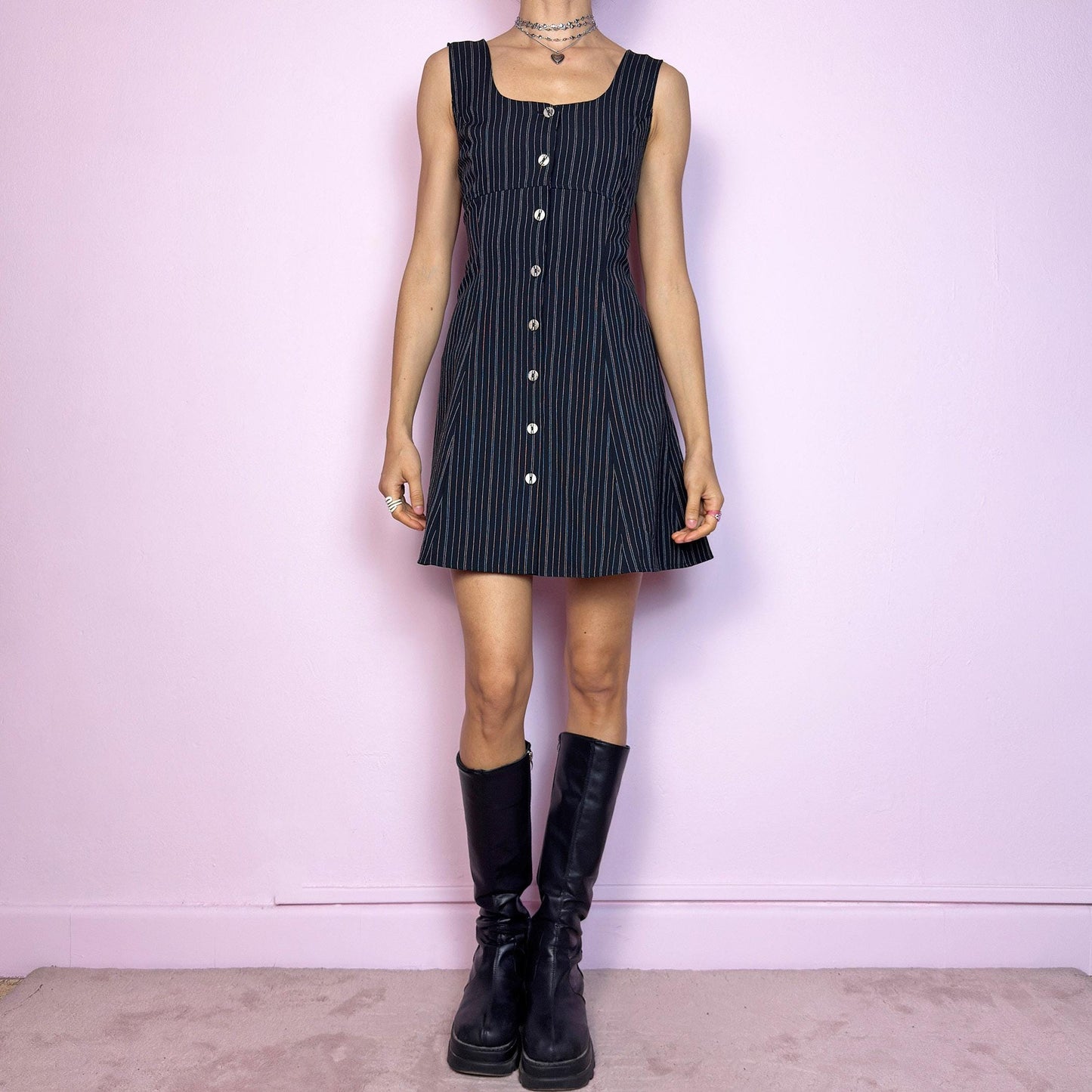 The Vintage 90s Black Pinstripe Mini Dress is a timeless piece with a flirty twist. This sleeveless dress features a black base with fine pinstripes, a fitted bodice with a square neckline, and a full front button closure. The slight A-line silhouette flatters the waist while keeping the vibe playful and polished. Ideal for 90s office-core and preppy looks. Excellent vintage condition.