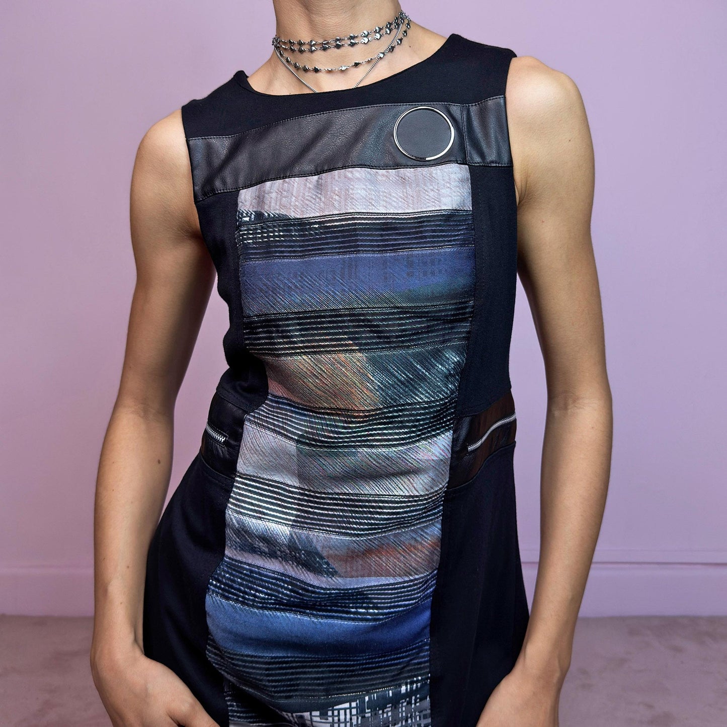 The Y2K Deconstructed Abstract Mini Dress is a futuristic and artsy statement piece. This vintage 2000s mini dress features a bold multicolor abstract panel at the front, contrasted with black side panels and leather-look trim. Designed with metallic ring hardware at the shoulder and waist for a deconstructed vibe. The silhouette is sleek and fitted, ideal for experimental streetwear or techwear-inspired edits. A unique piece for those who love unconventional details and 2000s aesthetics.