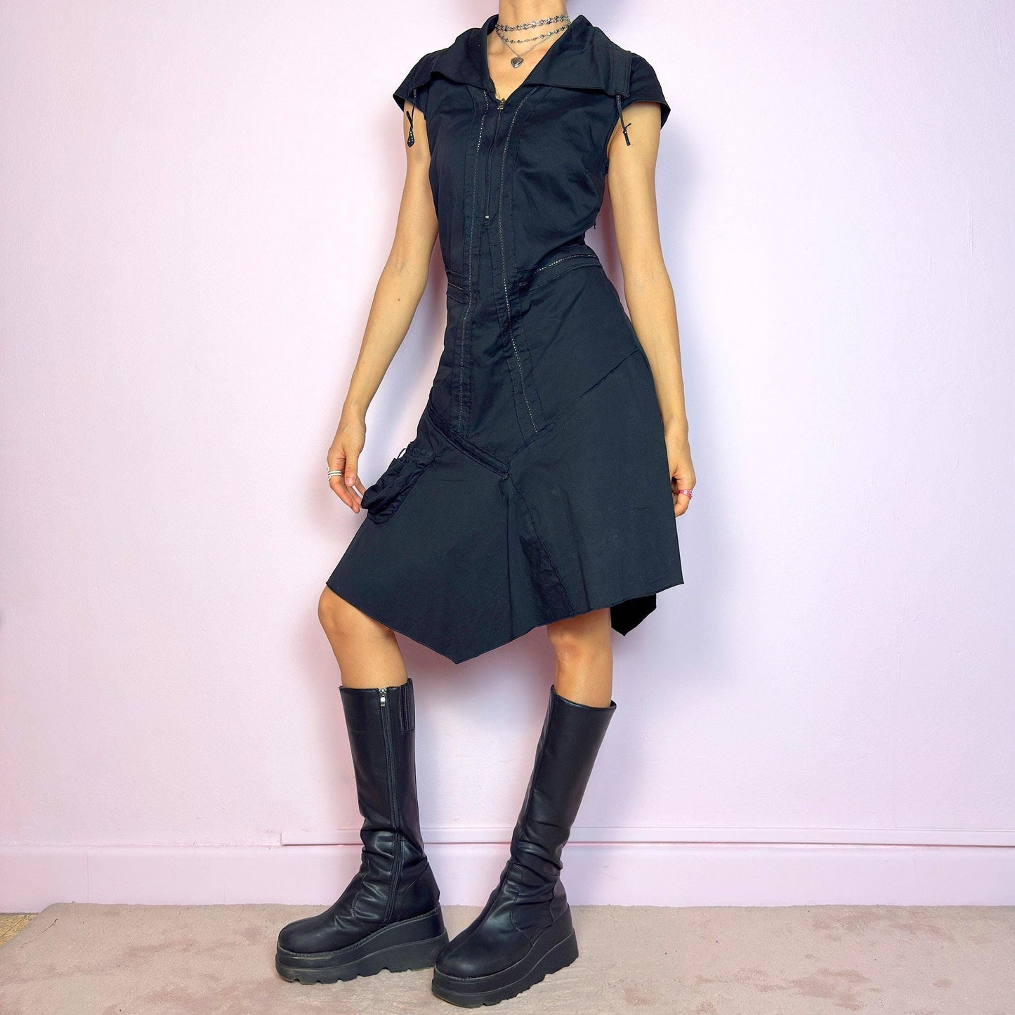 This vintage 2000s black techwear dress features cap sleeves, a dramatic asymmetric hem, and sculptural paneling for a bold silhouette. Made from a stretchy fabric, it includes a side zip closure and ruched utility pocket. Decorative topstitching and a funnel-style collar with drawstrings elevate the structure. Mid-length and lightweight, perfect for summer. A sleek statement in futuristic edge. Great vintage condition.