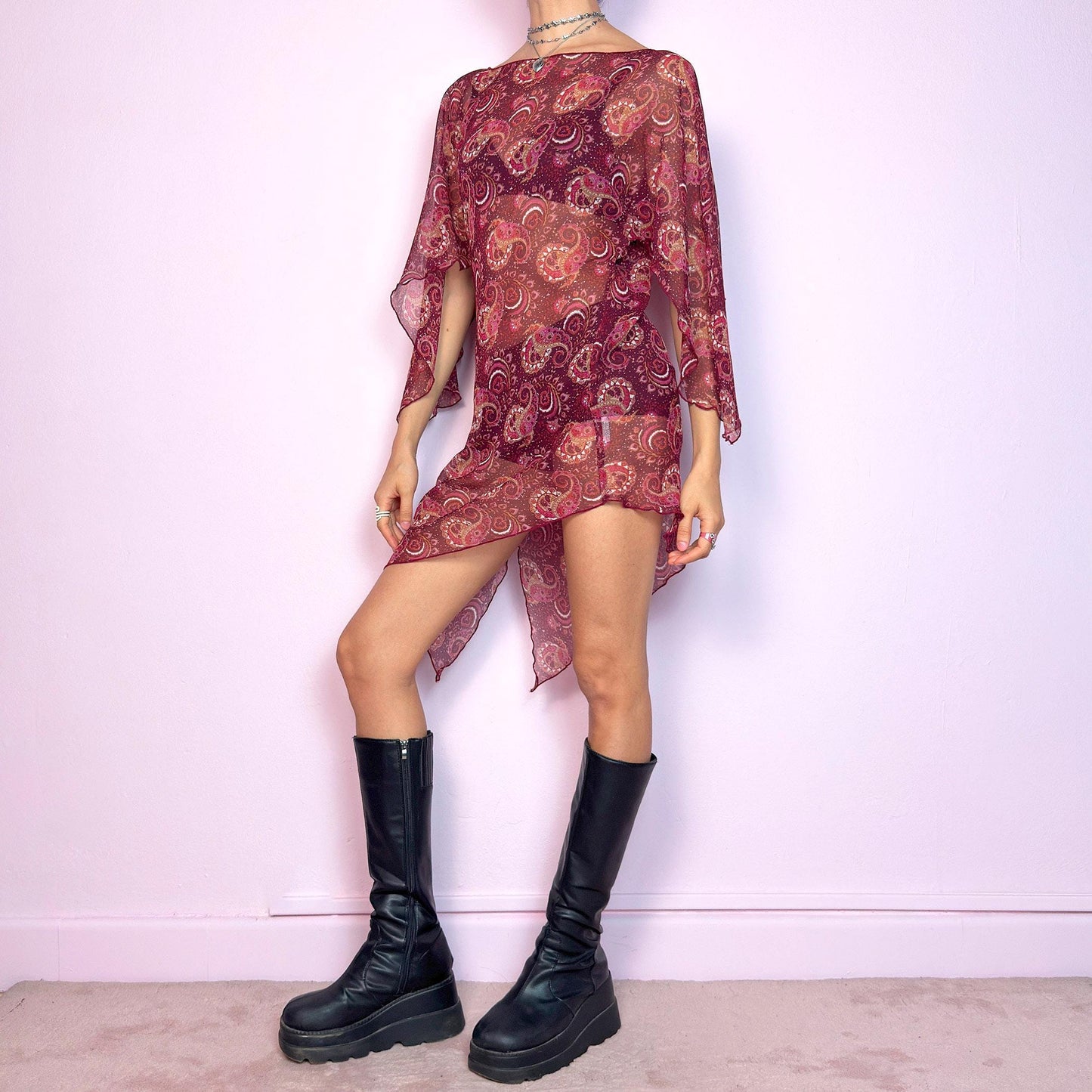 This vintage 2000s mini dress features a sheer burgundy paisley print, wide butterfly sleeves, and an asymmetric hem. Cut from lightweight fabric with no stretch, it drapes fluidly and falls mid-thigh with high side slits. Unlined and semi-transparent, perfect for layering or worn bold. A romantic Y2K silhouette with bohemian and fairycore energy—effortless, floaty, and made for summer nights. Great vintage condition.