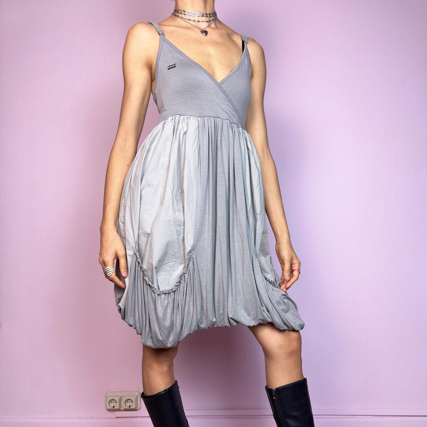 This vintage 2000s mini dress features a soft grey palette, deep wrap V-neckline, and empire waist with adjustable straps and light stretch. The voluminous bubble hem and oversized ruched pockets create sculptural movement and playful volume. Perfect for summer. A cyber-futuristic, deconstructed silhouette—airy, offbeat, and effortlessly cool. Excellent vintage condition.