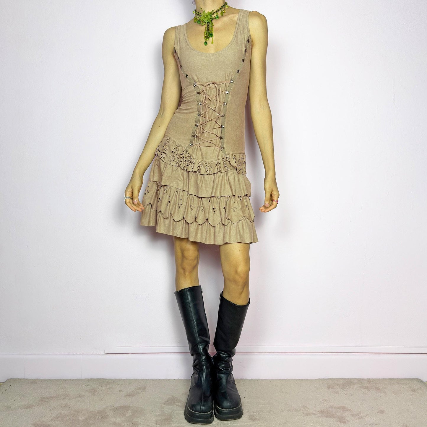 This vintage 2000s mini dress comes in soft beige with a scoop neckline, corset lace-up front, and stretchy fit. The drop waist leads to layered ruffle tiers with eyelet cutouts and scalloped hems. A fairy-meets-western Y2K silhouette—fitted on top, flirty on the bottom. Perfect for casual summer days or standout festival looks. Great vintage condition.