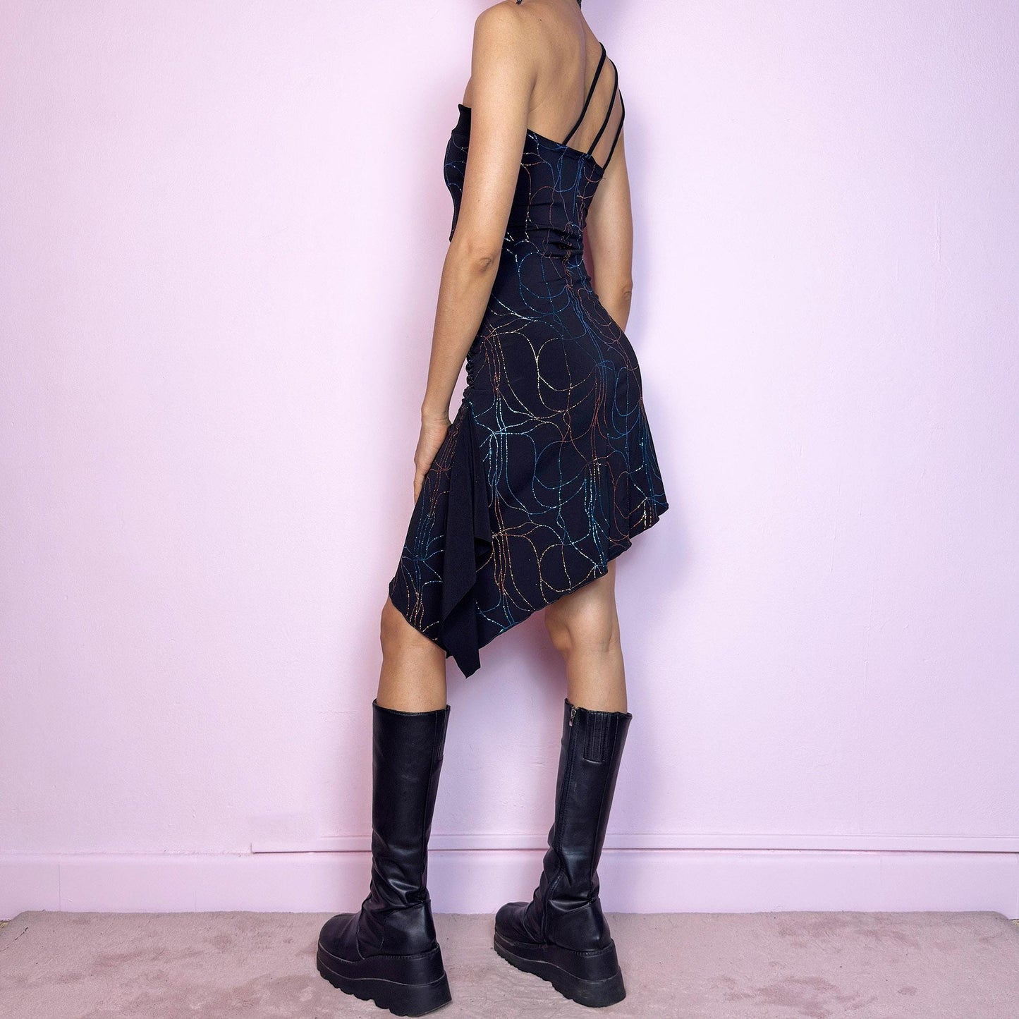 This vintage 2000s mini dress features a stretchy black base with multicolor glitter swirls, an asymmetric hem, and triple strap detail at one shoulder. The bodycon silhouette with side ruching hugs the form effortlessly. Pull-on style with no closures. A bold Y2K party piece with cyber-sleek energy—made for summer nights, raves, and standout moments. Made in Spain. Excellent vintage condition.