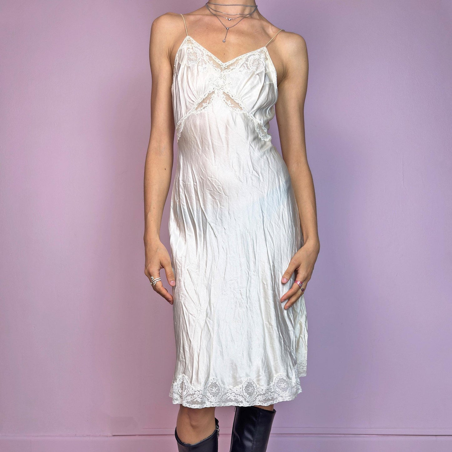 This vintage cream midi slip dress is likely from the 1940s–1950s, crafted from satin-style fabric with intricate floral lace at the bust, waist, and hem. Features a soft V-neckline, thin non-adjustable straps, and a body-skimming bias cut for graceful movement. Falls below the knee with a fluid, vintage silhouette. A rare, romantic undergarment with timeless elegance—ideal for collectors, layering, or as an ethereal evening statement.