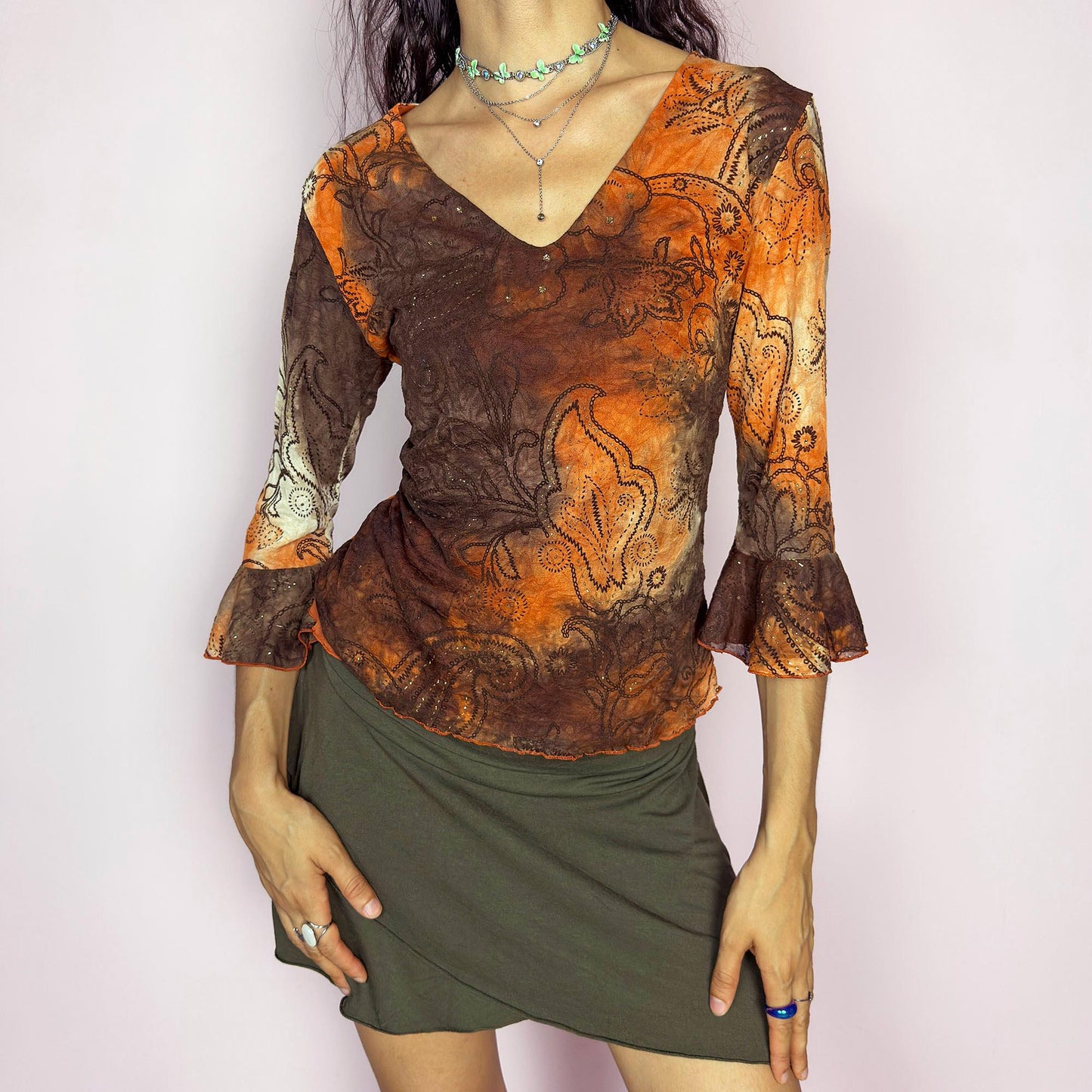This vintage 2000s mesh top features semi-sheer three-quarter bell sleeves and a deep V-neckline. The fitted silhouette is printed with a burnt orange and brown tie-dye paisley motif, accented by fine gold glitter for subtle shimmer. Made in France, it’s a dreamy piece for romantic, boho, or fairy grunge wardrobes. Made from stretch polyester blend. Excellent vintage condition.