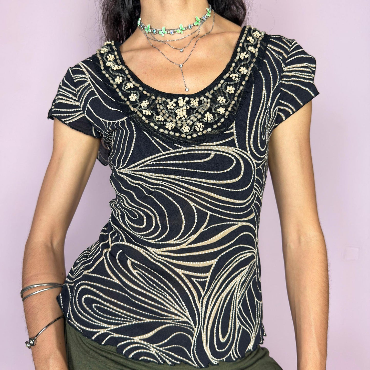 This vintage 2000s black semi-sheer mesh top features a fluid beige swirl print and sculptural wooden beadwork along the neckline. Slit cap sleeves enhance movement and lightness. A standout for summer nights, cruise escapes, or warm-weather layering. The fitted cut channels Y2K sensuality with artisanal edge. A collectible piece from a French brand. Made of lightweight polyamide. Excellent vintage condition.