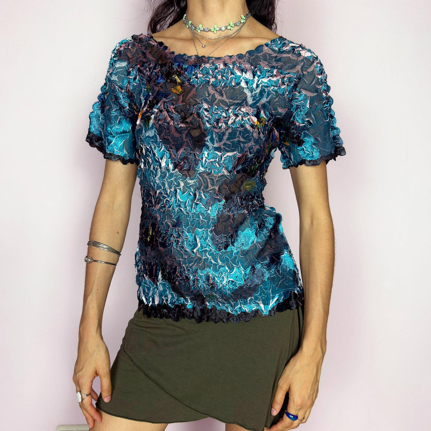 This vintage 90s avant-garde semi-sheer crinkle mesh top shimmers in shiny shades of teal, navy, and plum, with hints of white highlights. The pleated texture and short sleeves evoke playful elegance. Ideal for night outs, art parties, or expressive layering. A rare archival piece with pictorial, painterly brushstroke detail. Made of lightweight stretch fabric. Excellent vintage condition.