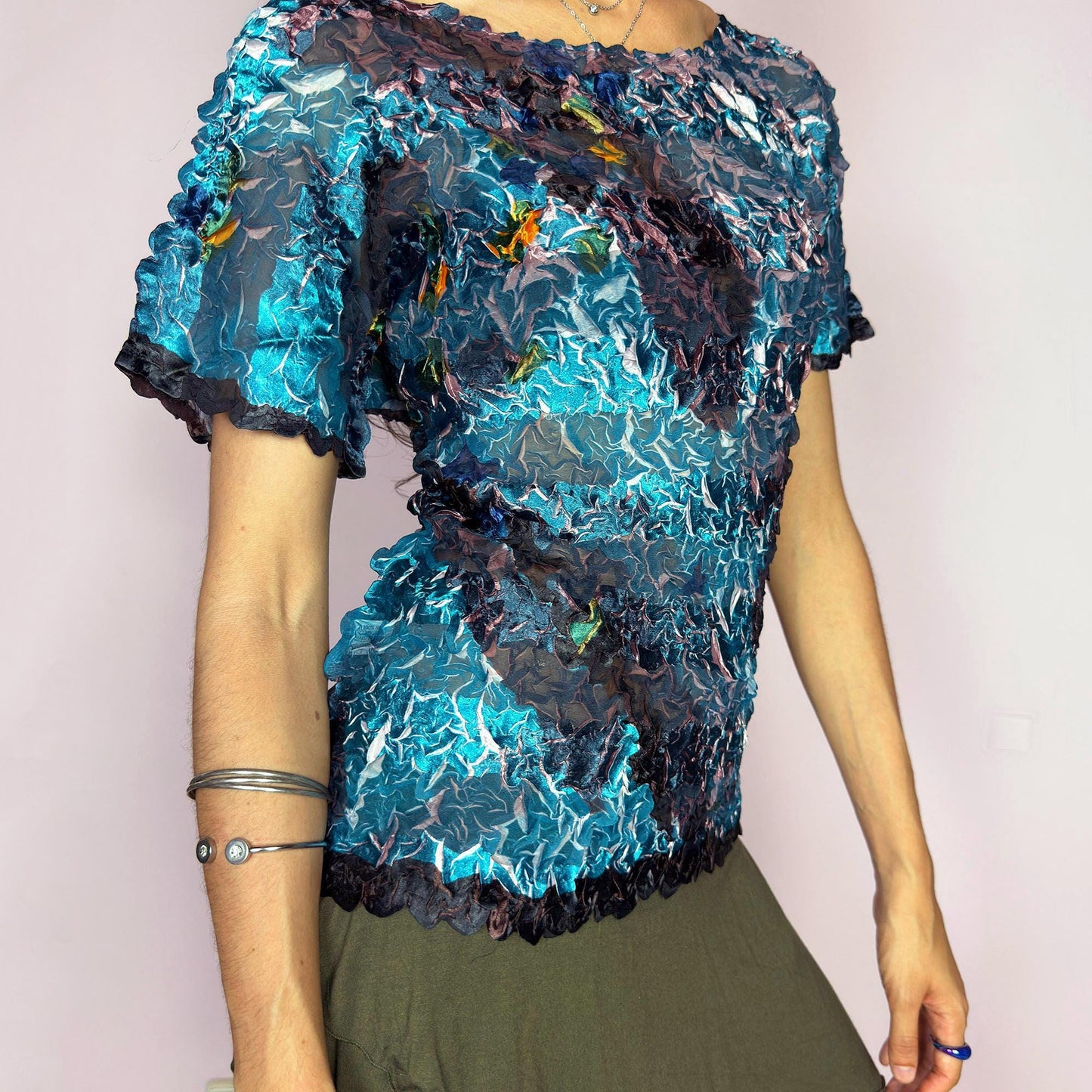 This vintage 90s avant-garde semi-sheer crinkle mesh top shimmers in shiny shades of teal, navy, and plum, with hints of white highlights. The pleated texture and short sleeves evoke playful elegance. Ideal for night outs, art parties, or expressive layering. A rare archival piece with pictorial, painterly brushstroke detail. Made of lightweight stretch fabric. Excellent vintage condition.