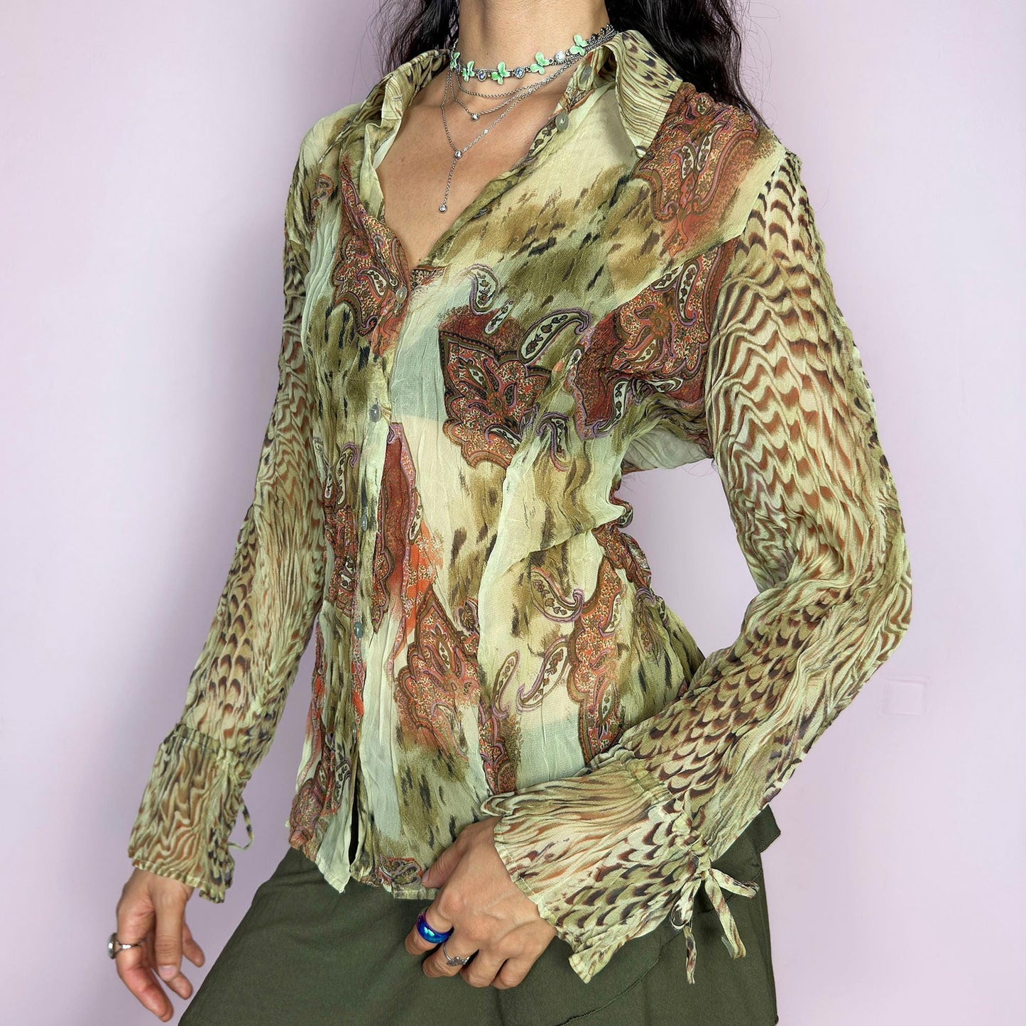 This vintage 2000s pleated sheer blouse blends soft sage green with wild paisley and animal-inspired prints in rust and brown. Features include tie details at the flared cuffs and a sharp pointed collar. A lightweight, breathable layer ideal for transitional styling, evening events, or a creative summer escapade in the Mediterranean. A rare, print-rich piece channeling bohemian and surrealist textures. Excellent vintage condition.