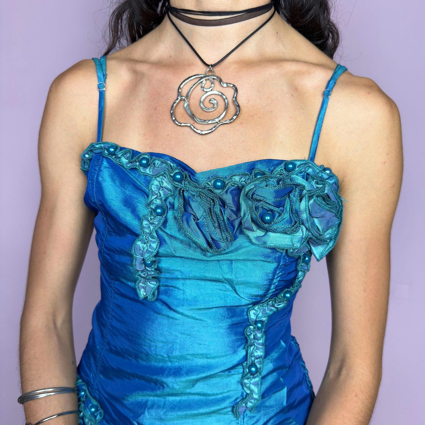 This vintage 2000s iridescent turquoise corset top features adjustable spaghetti straps, floral rosette appliqué, and beaded trim. The structured front sculpts the waist, while the ruched smocked back adds stretch and comfort. An asymmetrical hem and glossy finish elevate it for prom, weddings, or dreamy nights out. A romantic Y2K formal top that blends fairytale opulence with a bold, sculptural silhouette. Excellent vintage condition.