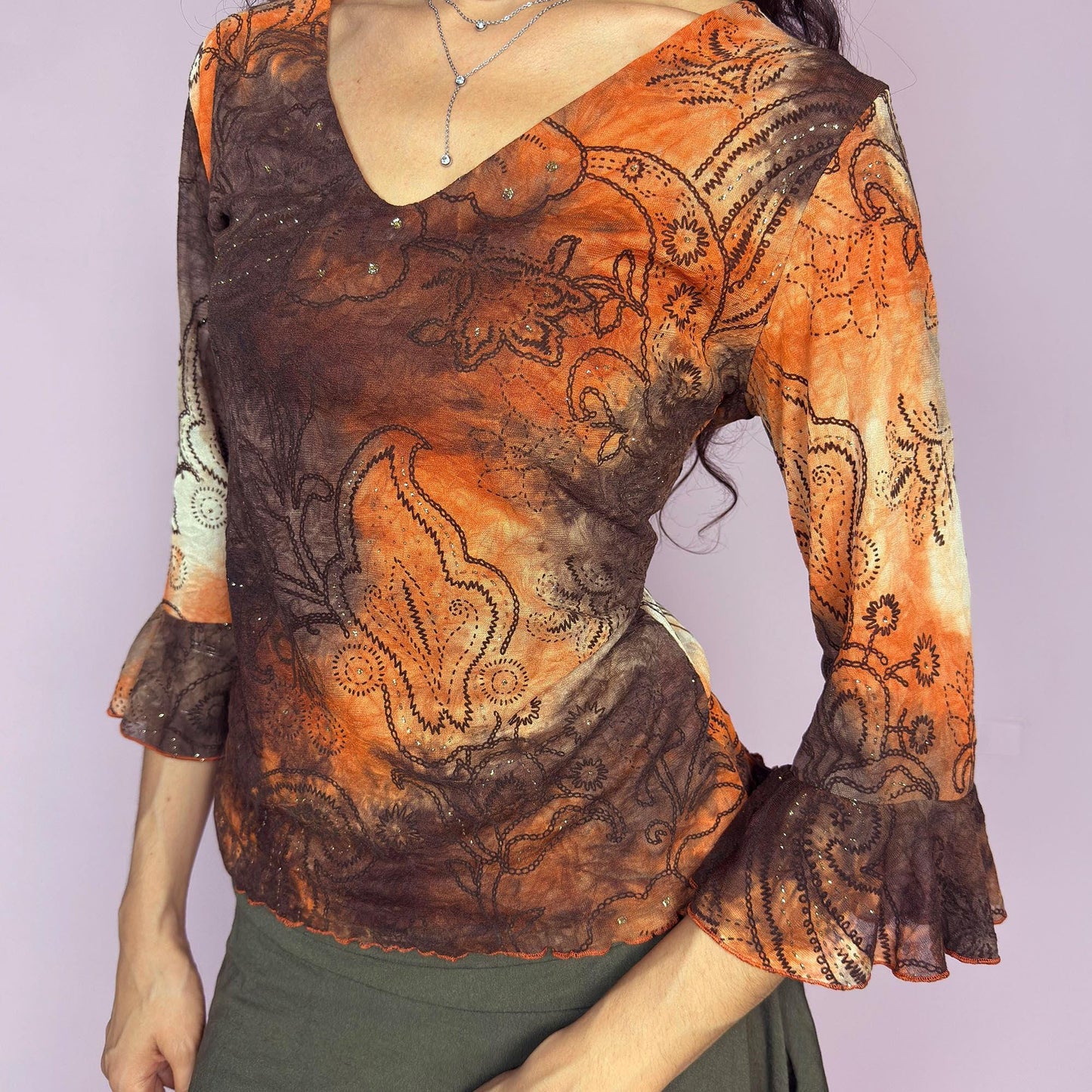 This vintage 2000s mesh top features semi-sheer three-quarter bell sleeves and a deep V-neckline. The fitted silhouette is printed with a burnt orange and brown tie-dye paisley motif, accented by fine gold glitter for subtle shimmer. Made in France, it’s a dreamy piece for romantic, boho, or fairy grunge wardrobes. Made from stretch polyester blend. Excellent vintage condition.