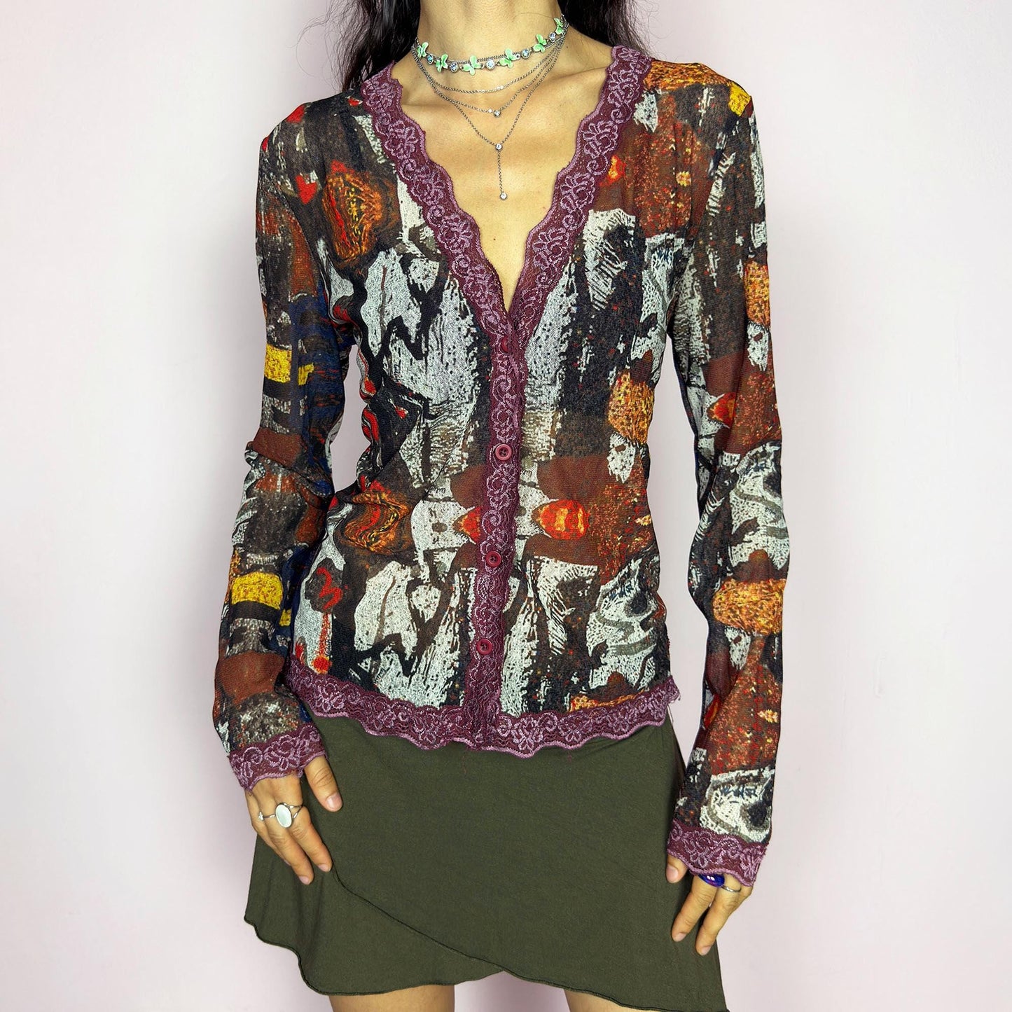 The vintage 2000s mesh sheer blouse features an abstract painting print in burnt orange, ochre, red, and charcoal. Made of stretch polyester mesh, it has long sleeves, a deep V-neckline trimmed in plum lace, and a tonal button front. This top is a rare avant garde piece with a romantic, artsy edge—perfect for chic events, layering, and transitional weather. Excellent vintage condition.