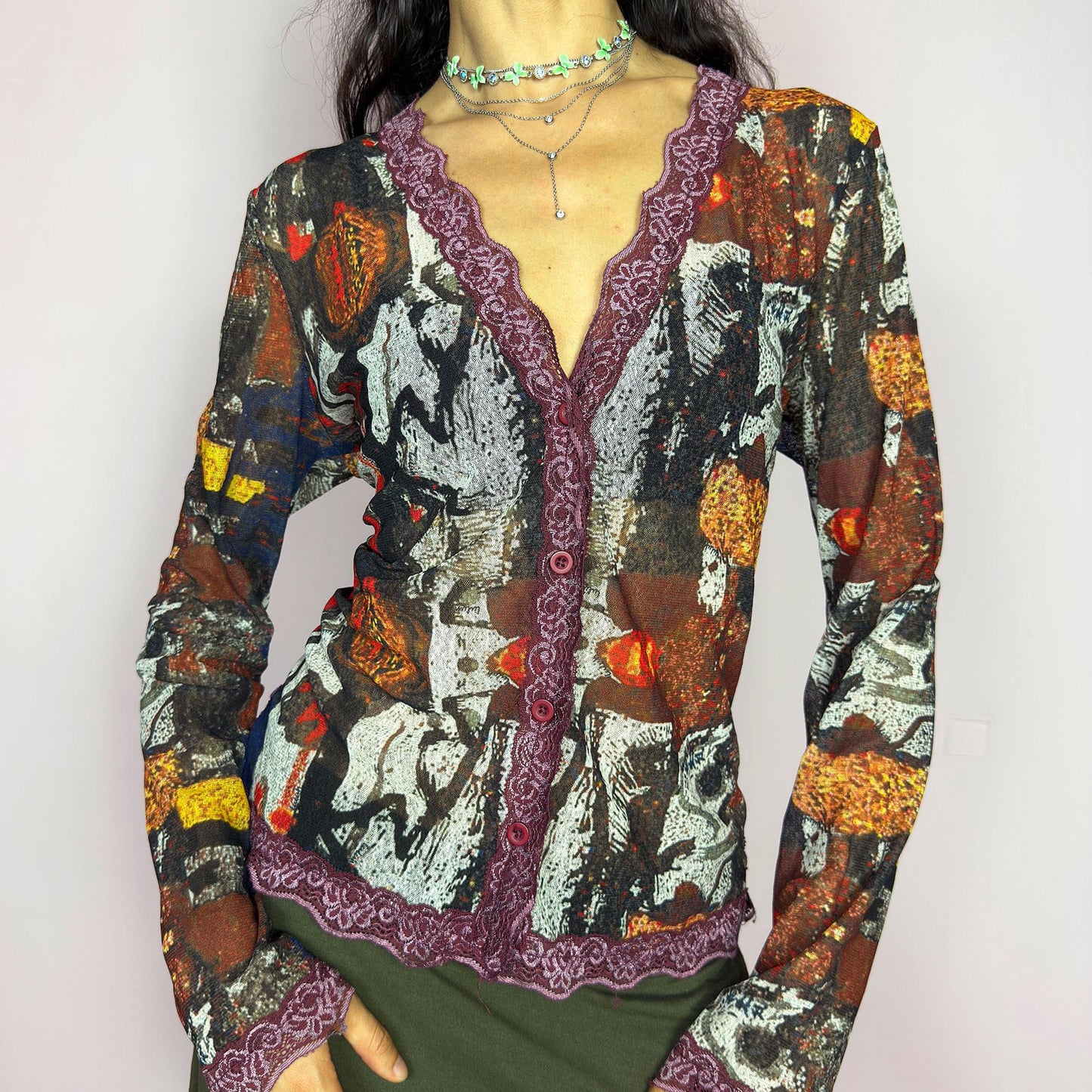The vintage 2000s mesh sheer blouse features an abstract painting print in burnt orange, ochre, red, and charcoal. Made of stretch polyester mesh, it has long sleeves, a deep V-neckline trimmed in plum lace, and a tonal button front. This top is a rare avant garde piece with a romantic, artsy edge—perfect for chic events, layering, and transitional weather. Excellent vintage condition.