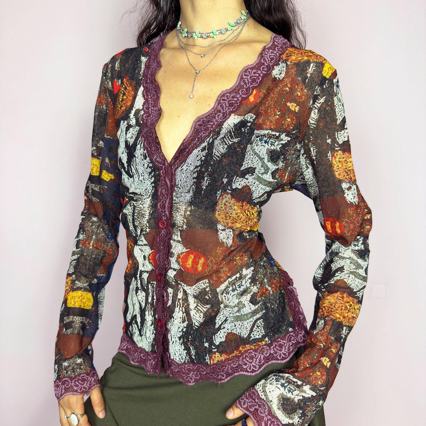 The vintage 2000s mesh sheer blouse features an abstract painting print in burnt orange, ochre, red, and charcoal. Made of stretch polyester mesh, it has long sleeves, a deep V-neckline trimmed in plum lace, and a tonal button front. This top is a rare avant garde piece with a romantic, artsy edge—perfect for chic events, layering, and transitional weather. Excellent vintage condition.
