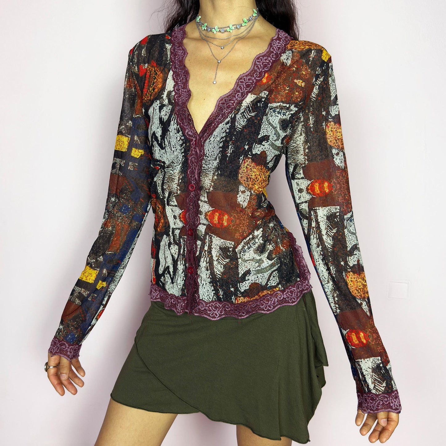 The vintage 2000s mesh sheer blouse features an abstract painting print in burnt orange, ochre, red, and charcoal. Made of stretch polyester mesh, it has long sleeves, a deep V-neckline trimmed in plum lace, and a tonal button front. This top is a rare avant garde piece with a romantic, artsy edge—perfect for chic events, layering, and transitional weather. Excellent vintage condition.