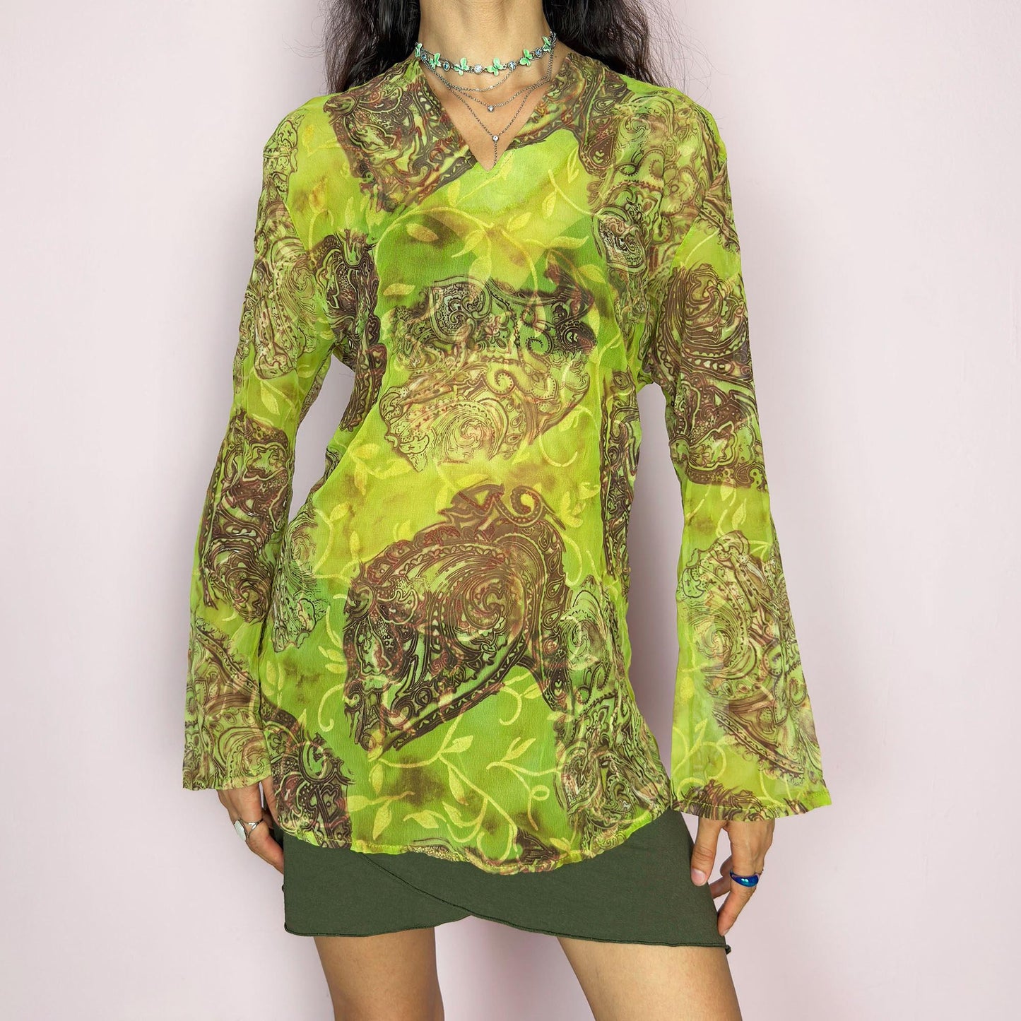 This vintage 2000s bohemian sheer green blouse casts a psychedelic glow with swirling brown paisley motifs and fluid draping. Flared long sleeves and a soft V-neckline evoke carefree elegance. Wear it layered at summer parties or as a lightweight, kaftan-inspired beach cover-up. Made in France from lightweight polyester. Excellent vintage condition.