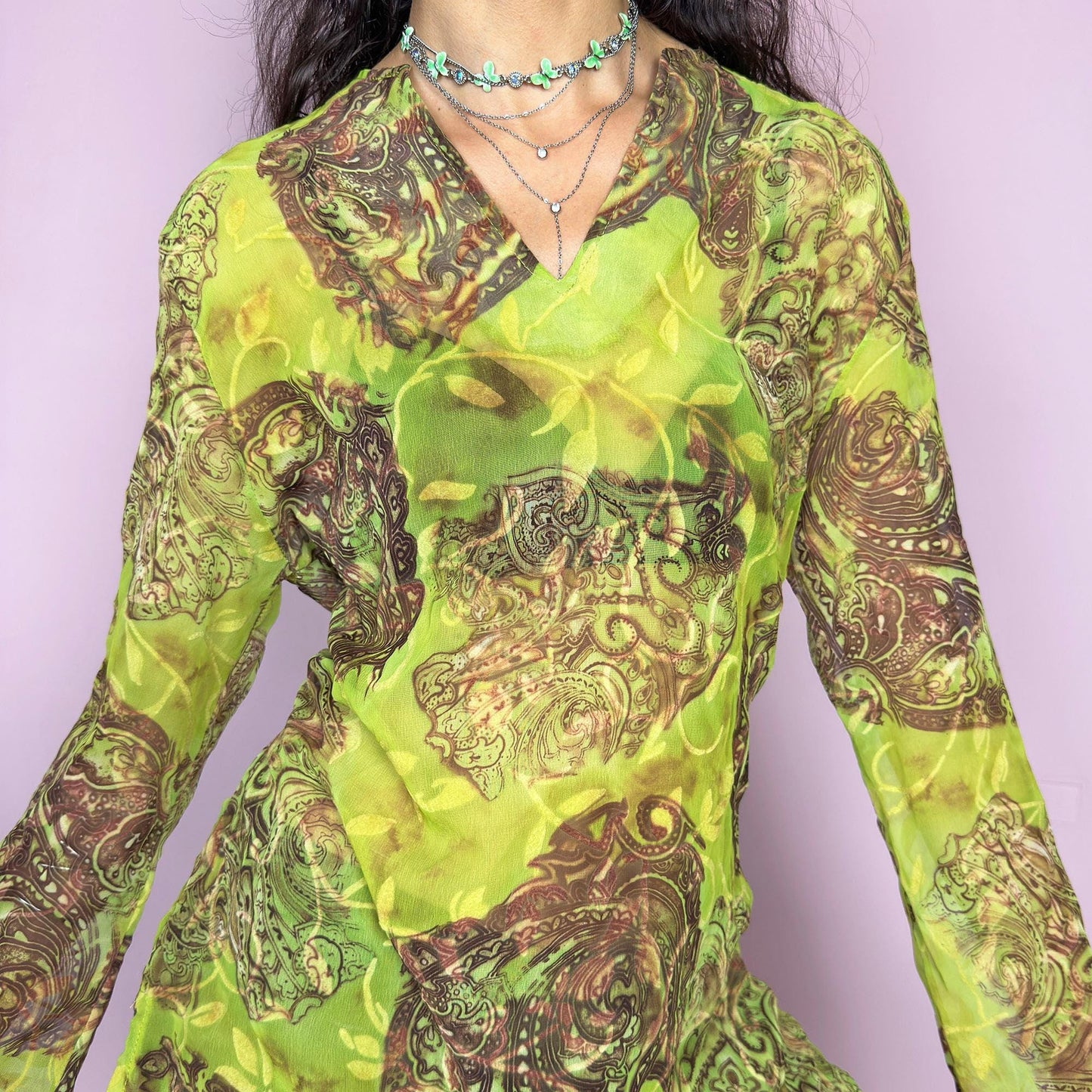 This vintage 2000s bohemian sheer green blouse casts a psychedelic glow with swirling brown paisley motifs and fluid draping. Flared long sleeves and a soft V-neckline evoke carefree elegance. Wear it layered at summer parties or as a lightweight, kaftan-inspired beach cover-up. Made in France from lightweight polyester. Excellent vintage condition.