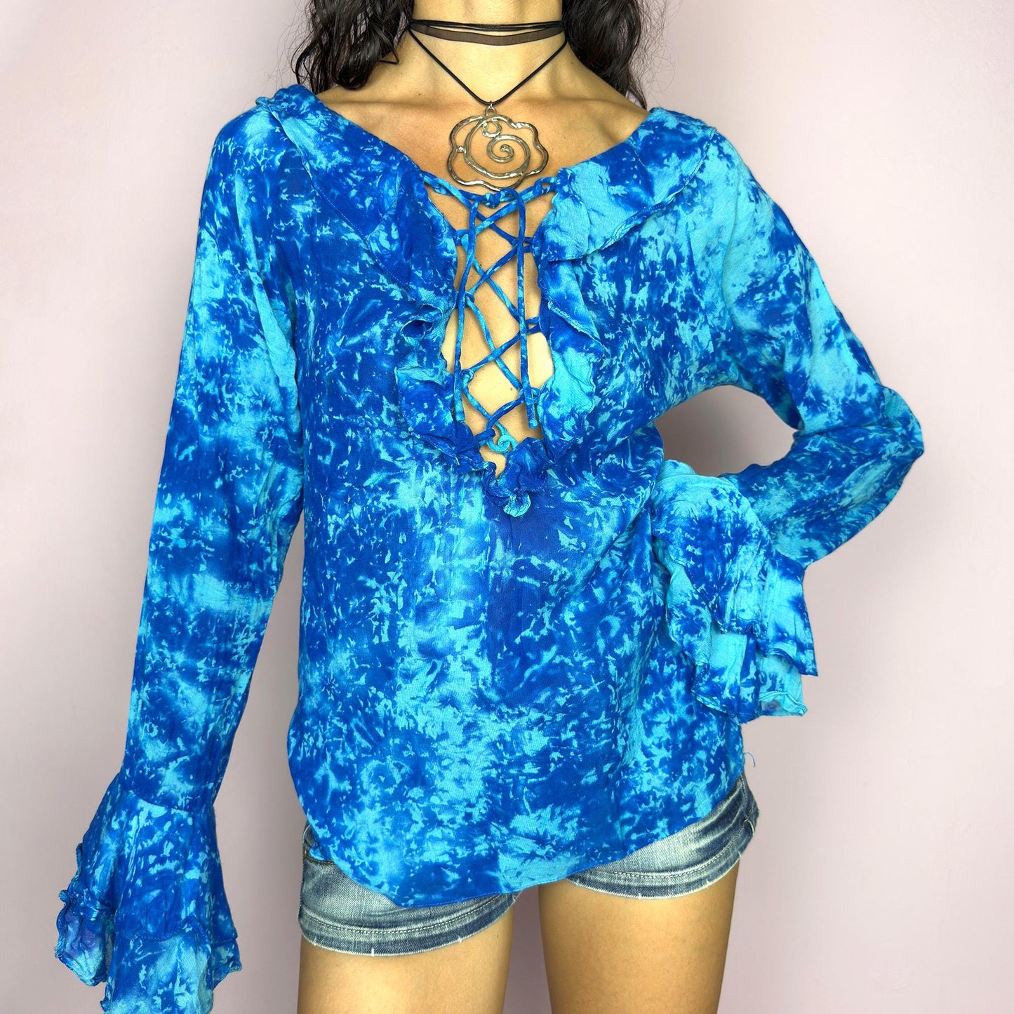 This vintage 90s blue tie dye top features dramatic ruffle cuffs, a deep lace-up neckline, and soft cotton-blend fabric in vibrant psychedelic tones. Designed with long sleeves it channels boho, hippie, and festival energy with bold originality. Lightweight and breathable, perfect for summer layering or statement styling. A rare archival blouse that captures wild 90s freedom. Excellent vintage condition.
