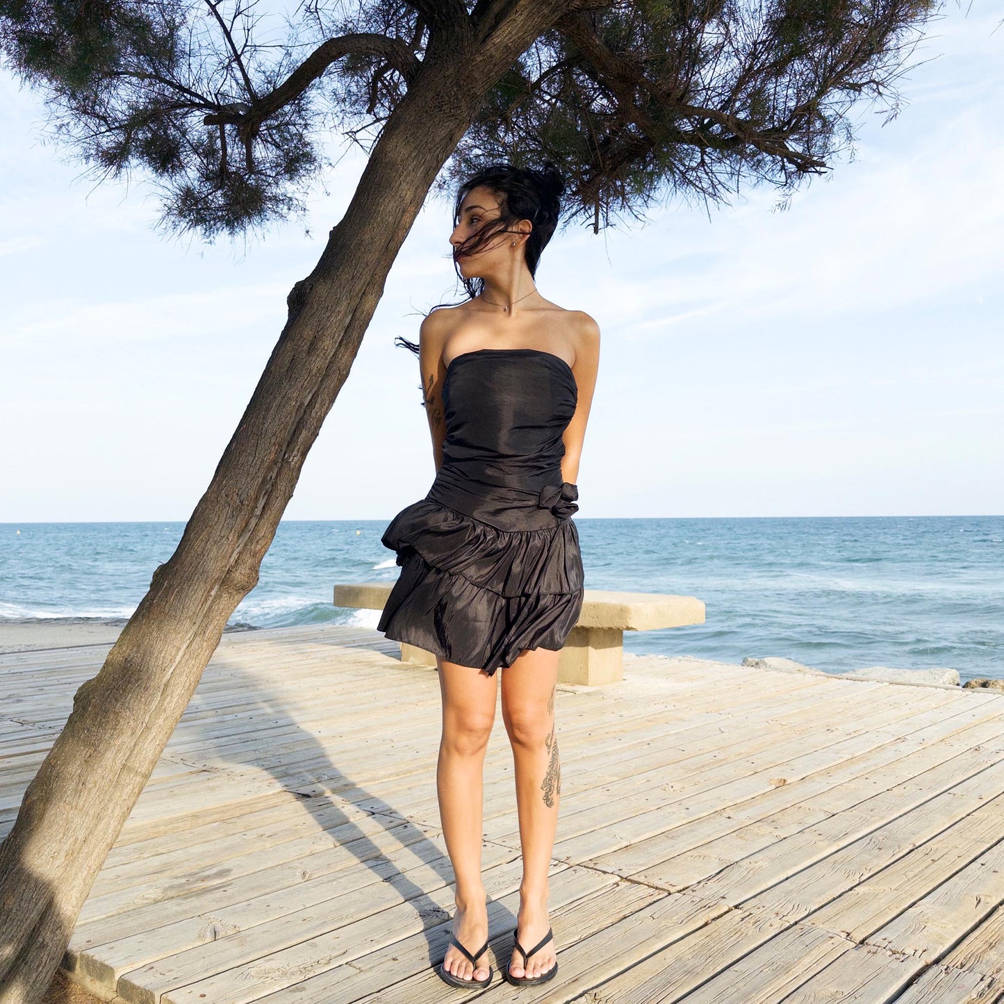 The vintage 90s black mini dress is a sculptural, strapless piece with ruched draping and voluminous double ruffle tiers. Made in Italy, it features a tie-back sash, shirred elastic panel, and side zip for a secure, flattering fit. Crafted from a polyester blend, it catches light effortlessly—ideal for summer nights, cocktail events, or rooftop parties. A super cute dress with high femme drama. Excellent vintage condition.
