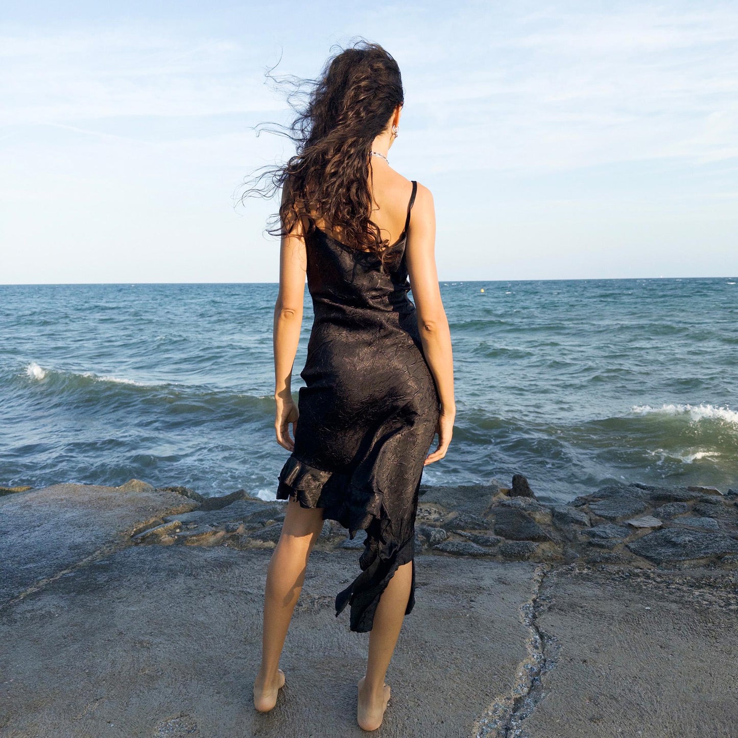 The vintage 2000s black slip dress is a made-in-France piece with crinkled texture and asymmetric ruffle hem. Its sculptural midi silhouette moves with quiet sensuality—ideal for gallery openings, formal nights, or late summer dates. A deconstructed Y2K shape that evokes avant-garde elegance, made to be seen without shouting. An archival dress crafted from a soft polyester blend. Excellent vintage condition.